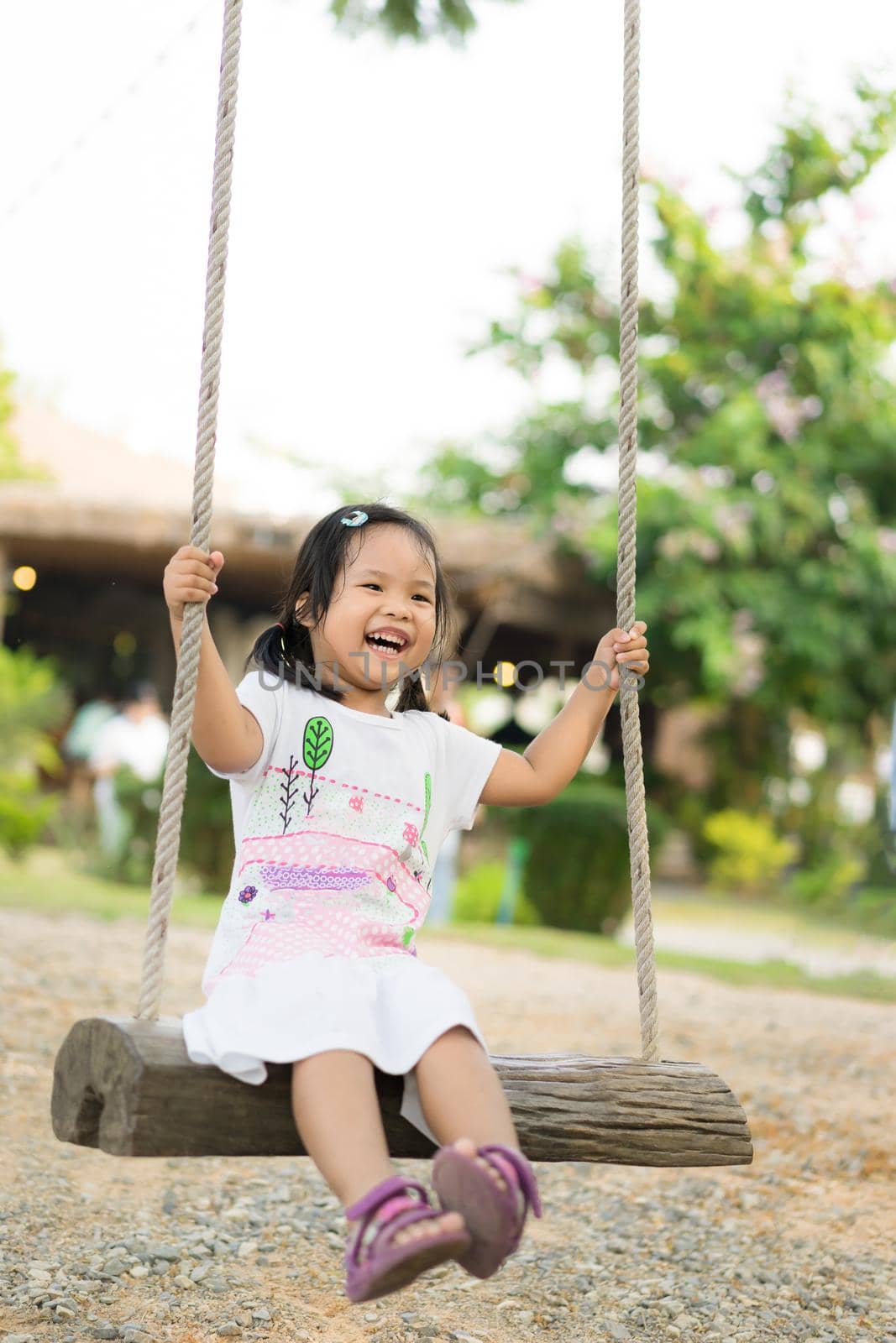Little girl in white dress sitting on a swing in the park