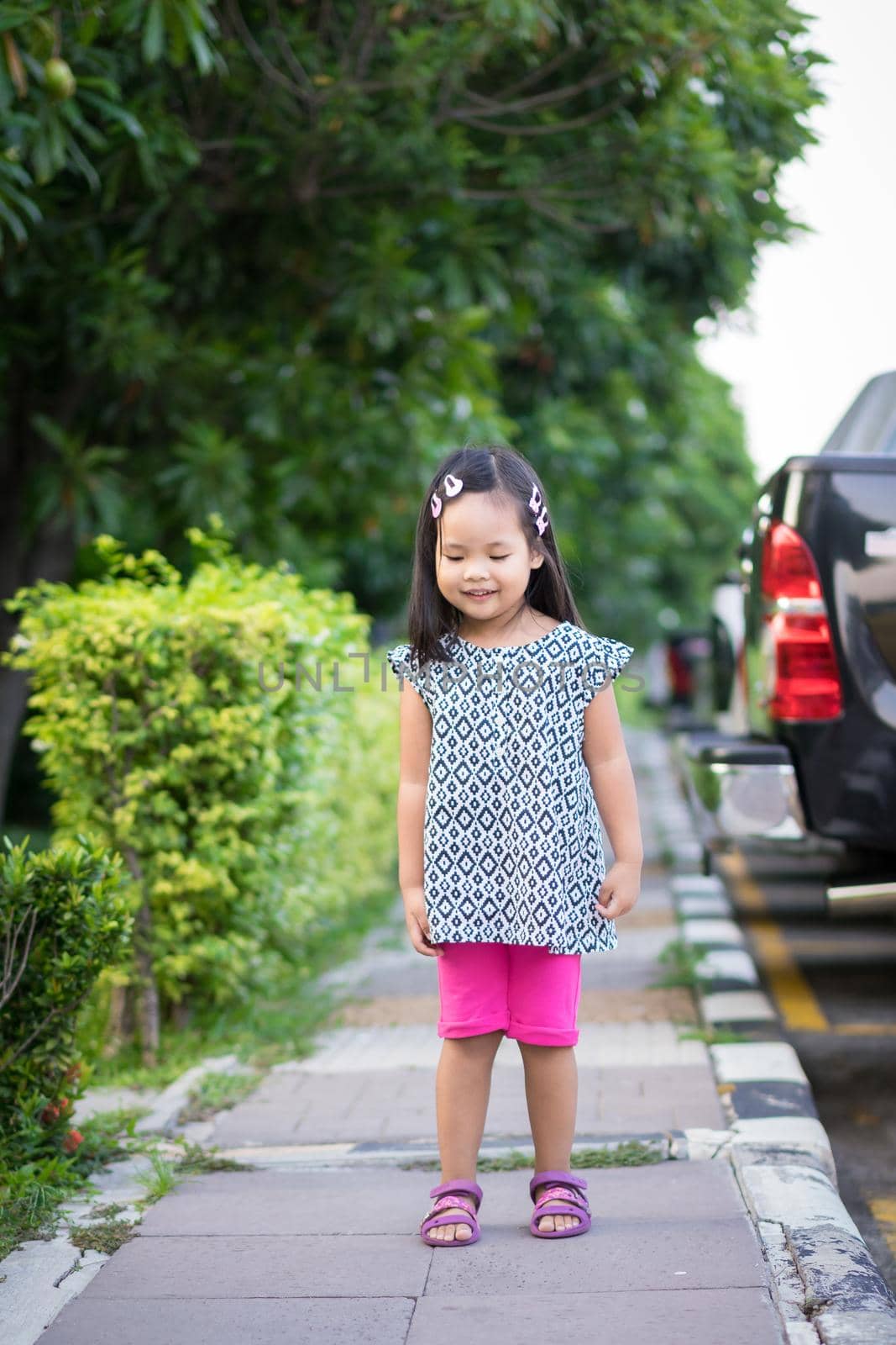 Portrait of happy asian little girl in dress standing on footpath in the park