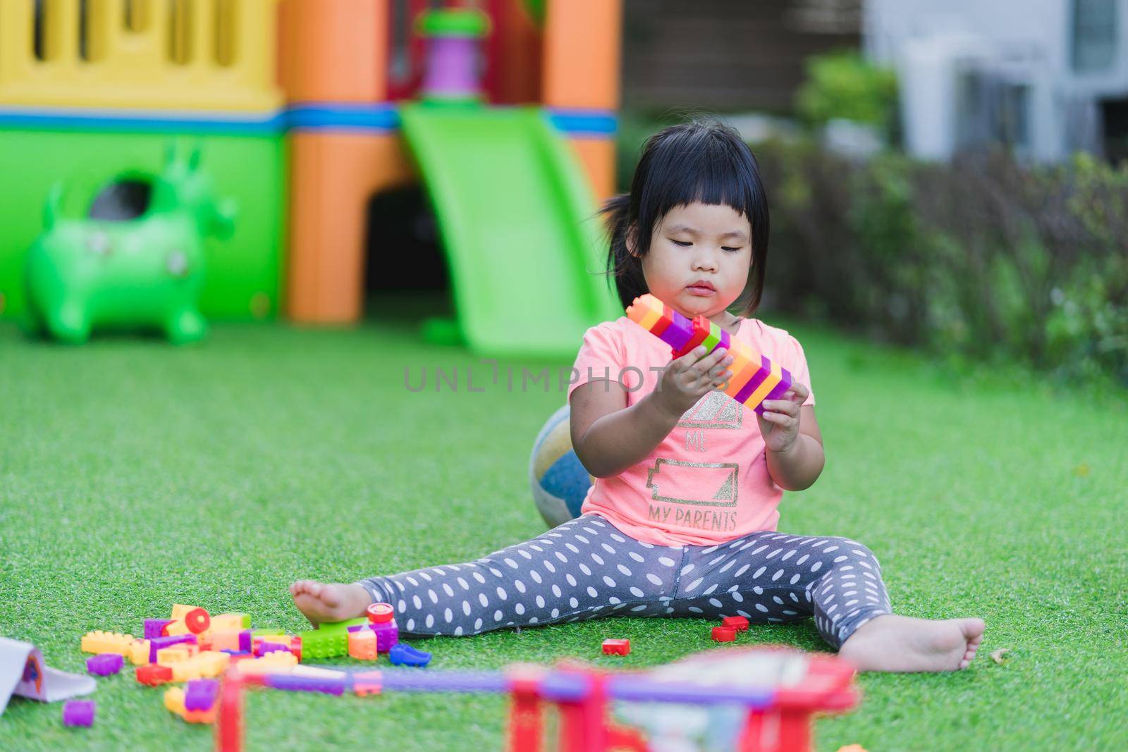 little girl playing toy colorful plastic blocks in playground by domonite