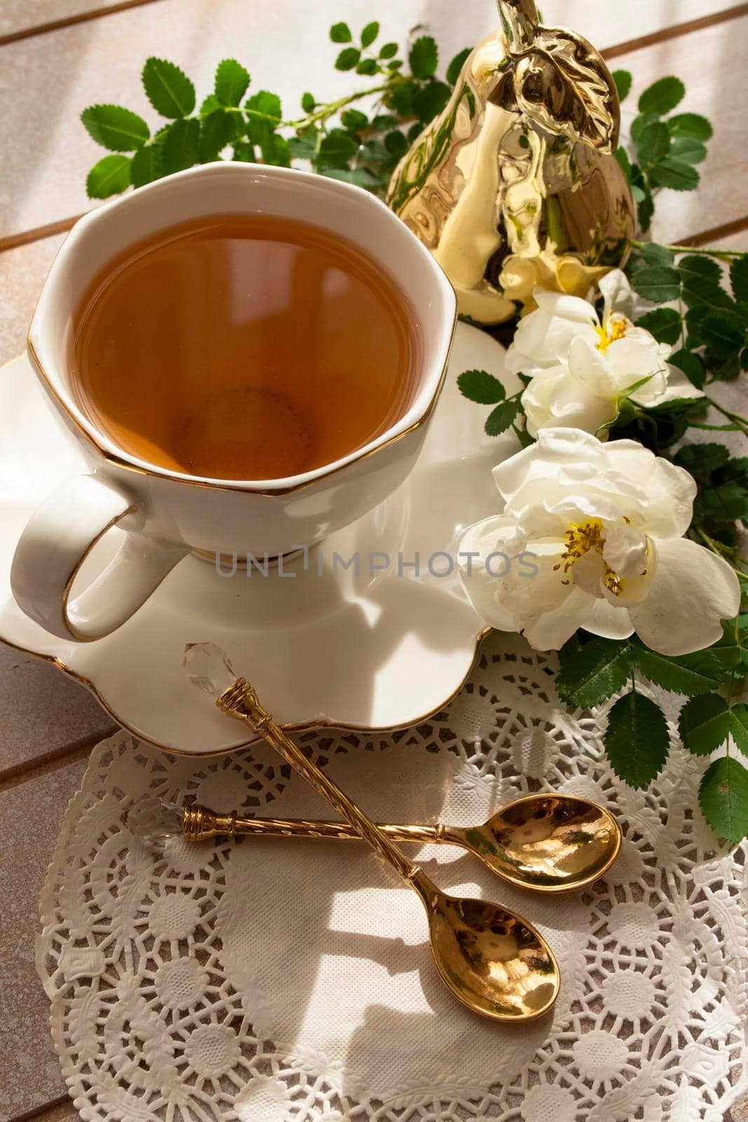 Tea in a china white cup and saucer, with white rose. Vertical image