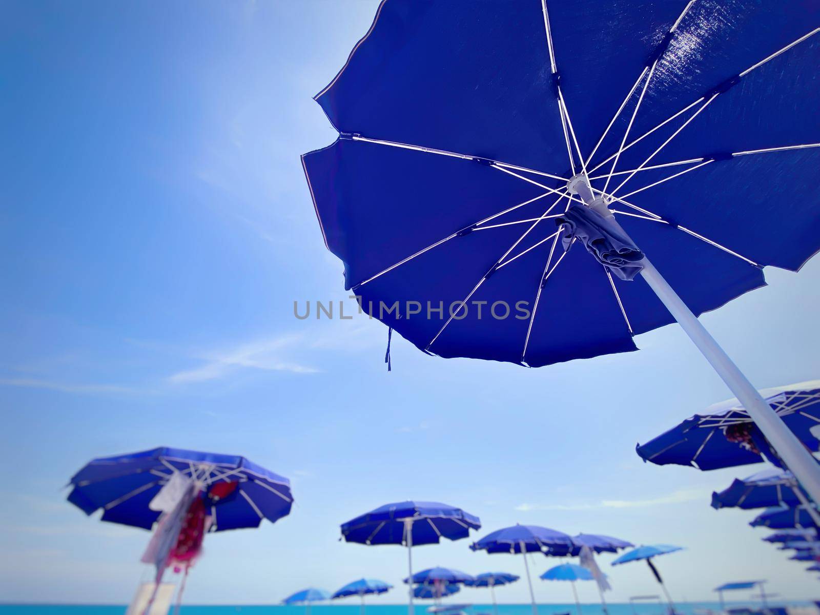 blue sun umbrellas open and arranged in rows at an Italian beach on a sunny summer day. Beach holidays in the summer and relaxation.