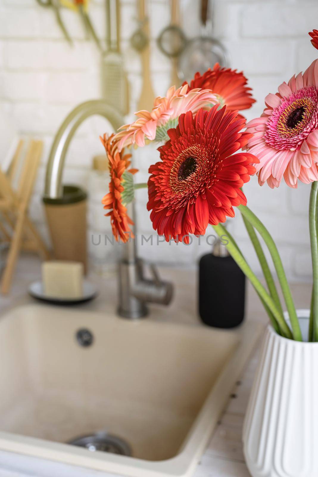 Rustic kitchen interior with white brick wall and white wooden shelves. Fresh gerbera flowers in a white vase