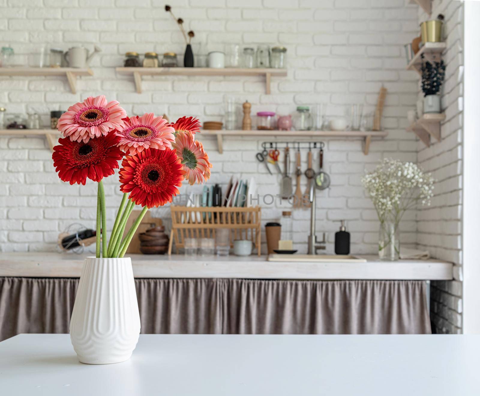 Rustic kitchen interior with white brick wall and white wooden shelves. Fresh gerbera flowers