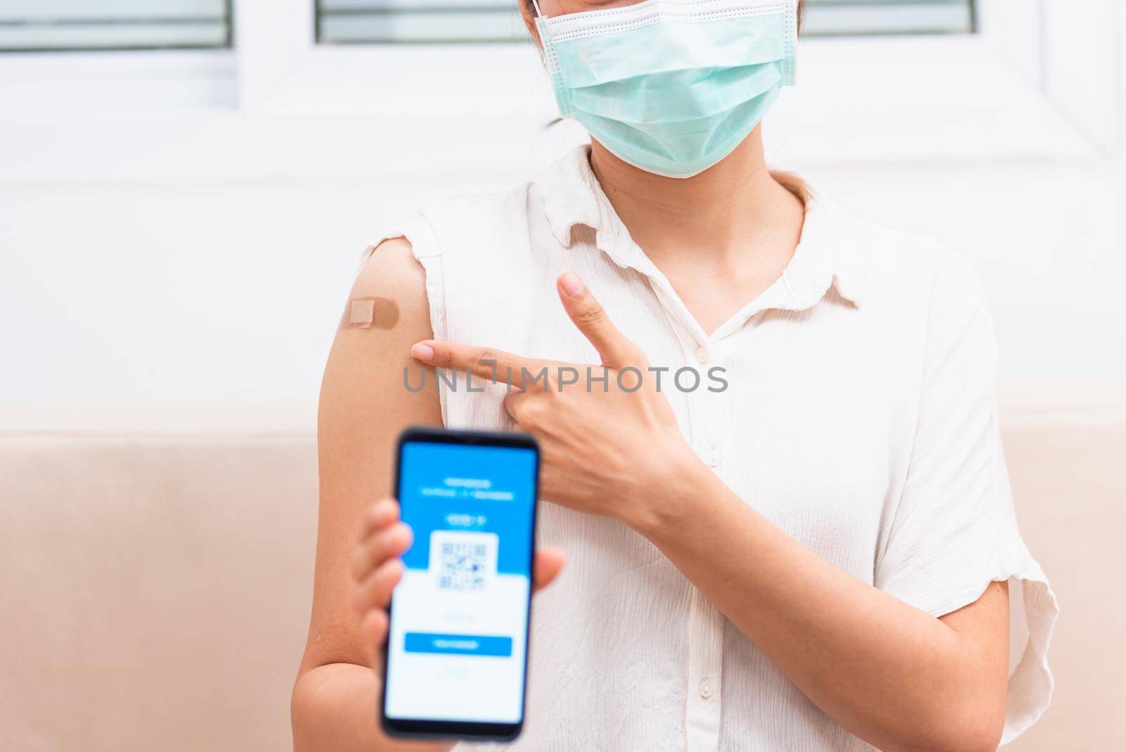 Asian young woman pointing to adhesive plaster on arm her vaccinated and showing app smartphone mobile digital screen vaccinated coronavirus (COVID-19) certificate after getting vaccine prevent