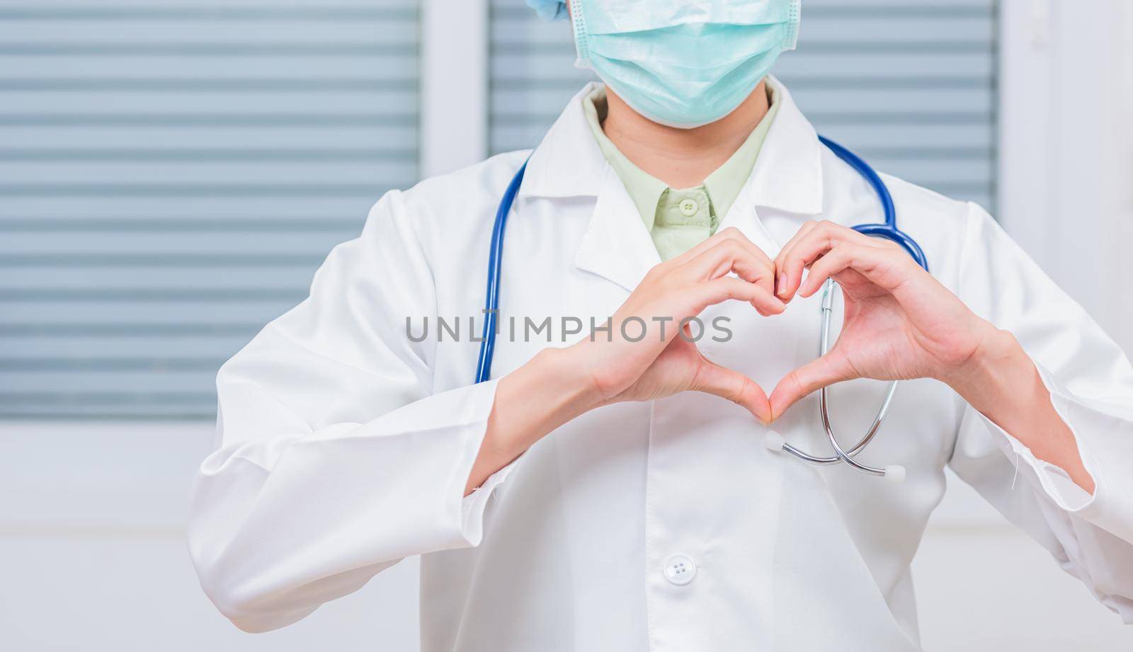 Closeup of doctor woman wearing white coat standing making heart finger shape, Doctor's hand sign, Healthy medical heart coronavirus concept