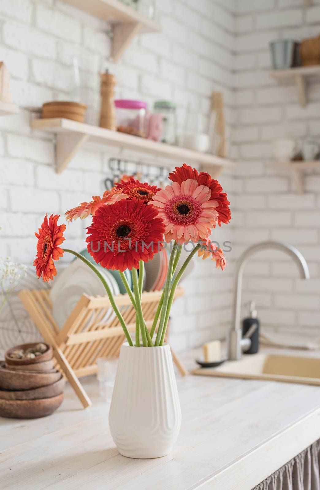 Rustic kitchen interior with white brick wall and white wooden shelves. Fresh gerbera flowers in a white vase