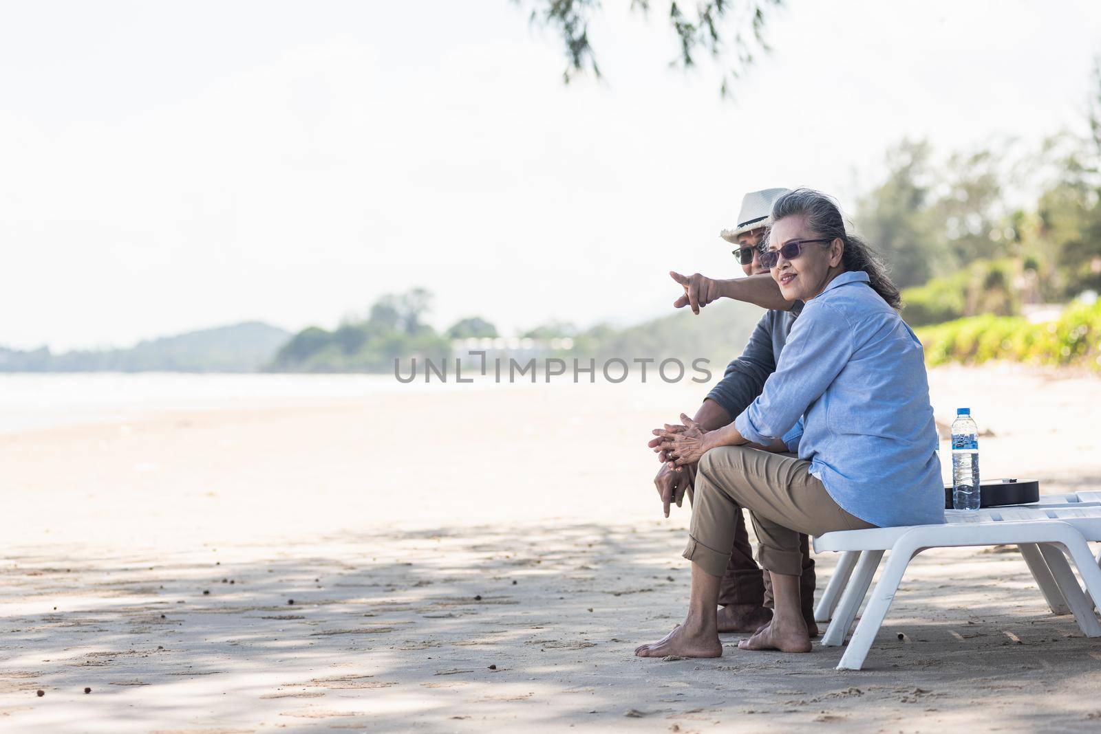 Happy Asian family, senior couple sitting on chairs with backs on beach travel vacation talking together by Sorapop