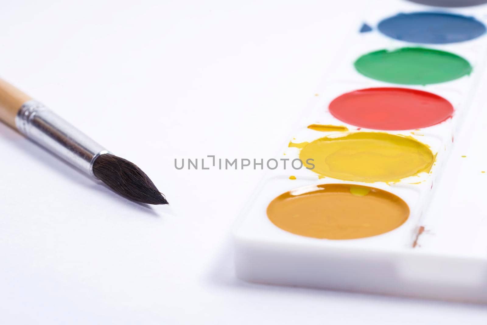 Colorful watercolor palette, top view of paintbrushes palette with brush on white paper background
