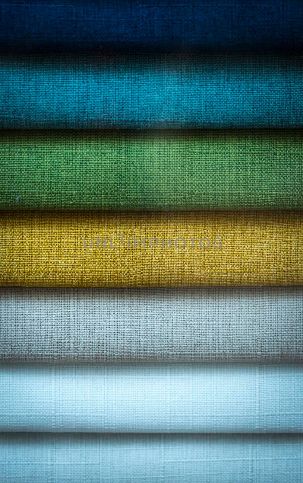 Rolls of colored fabric are neatly stacked in a row on the store shelves, close-up.