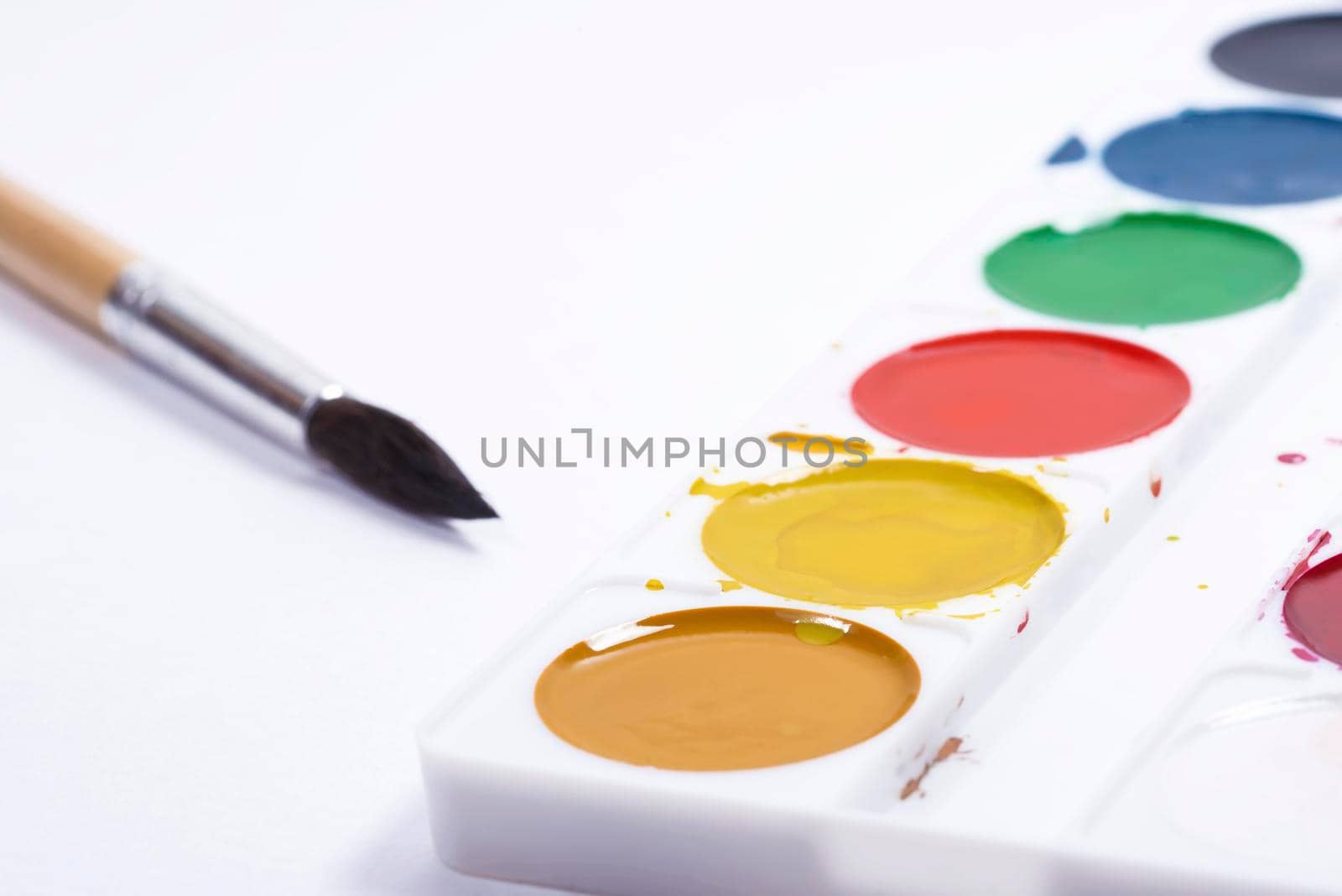 Colorful watercolor palette, top view of paintbrushes palette with brush on white paper background