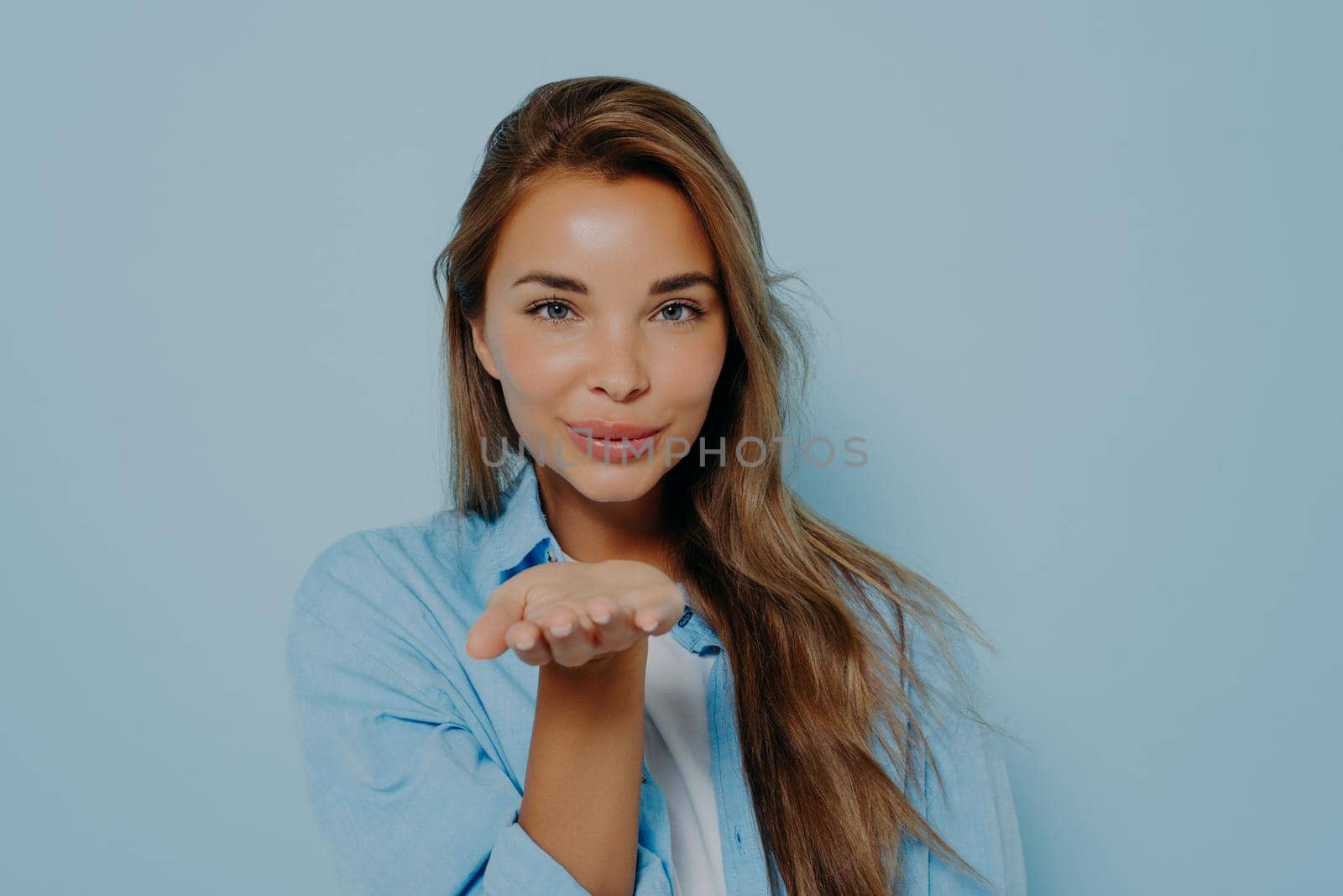 Woman blowing air kiss on light blue background by vkstock