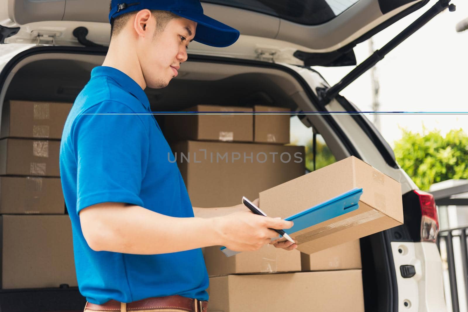 Asian young delivery man courier in uniform hold documents clipboard checking list parcel post boxes near a car for service shipment to customer, Online shopping service concepts