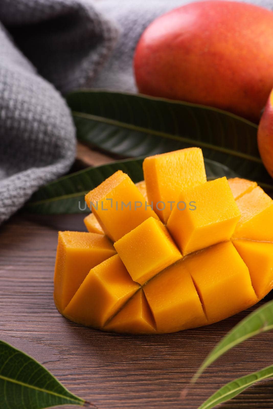 Mango. Close up of fresh ripe mango fruit with leaves over dark wooden table background with green leaves.