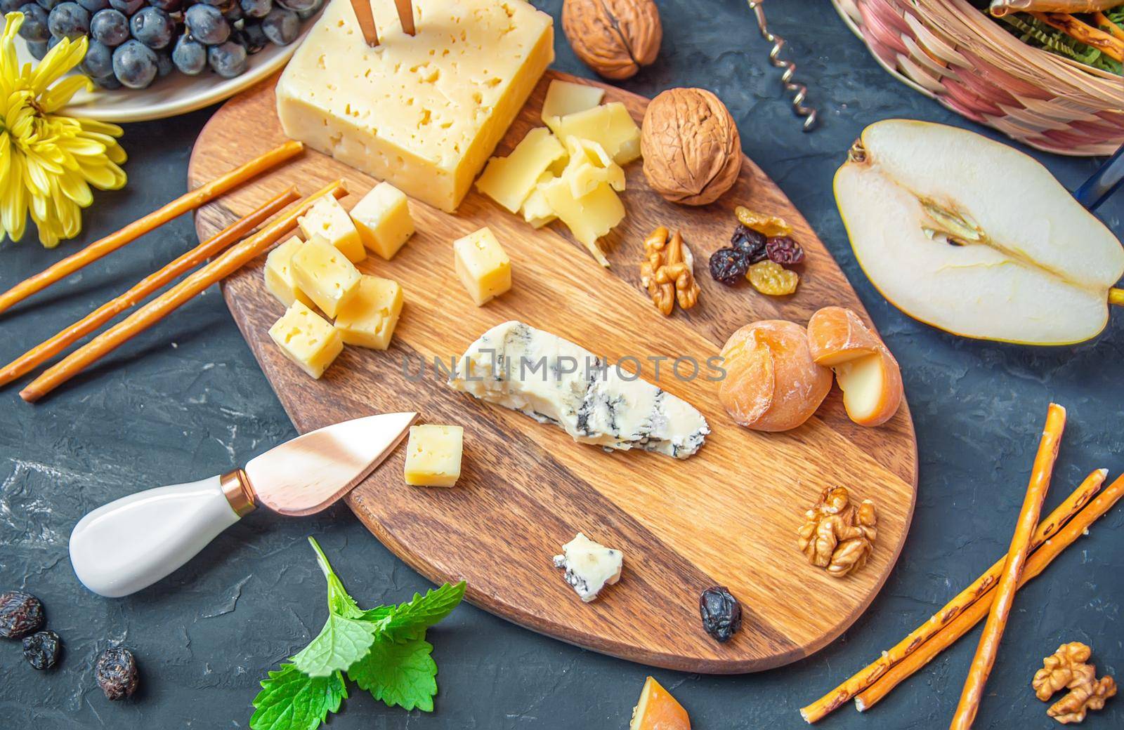 Cheese plate from different kind of cheese - Emmental, Homemade, Parmesan, blue cheese, bread sticks, walnuts, raisin, pear, grapes on a table by Estival