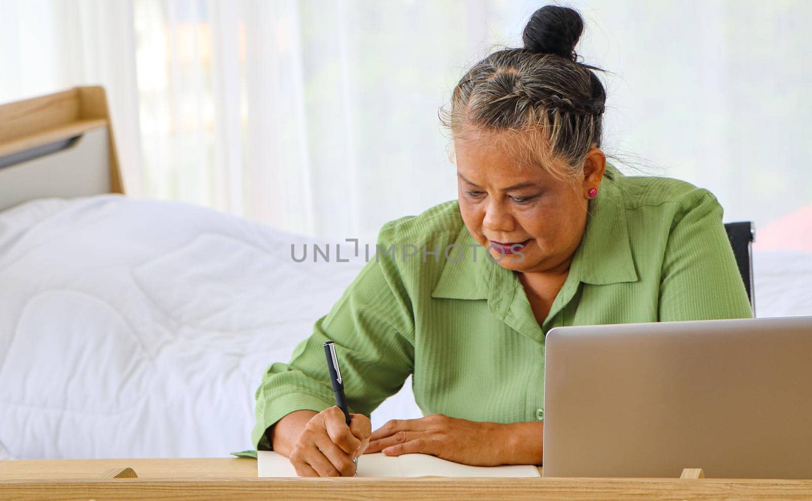 Senior woman retiring Asian Work, write and use the computer at the desk in the relaxing room. And working at the home of retirement