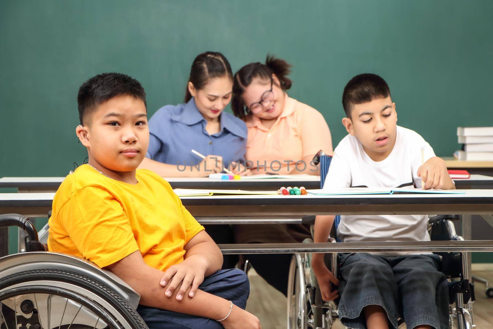 Asian disabled children Or, an autistic child learns to read, write, and train their hand and finger muscles with a teacher at their classroom desk. Concentrate and smile Happy disability kid concept