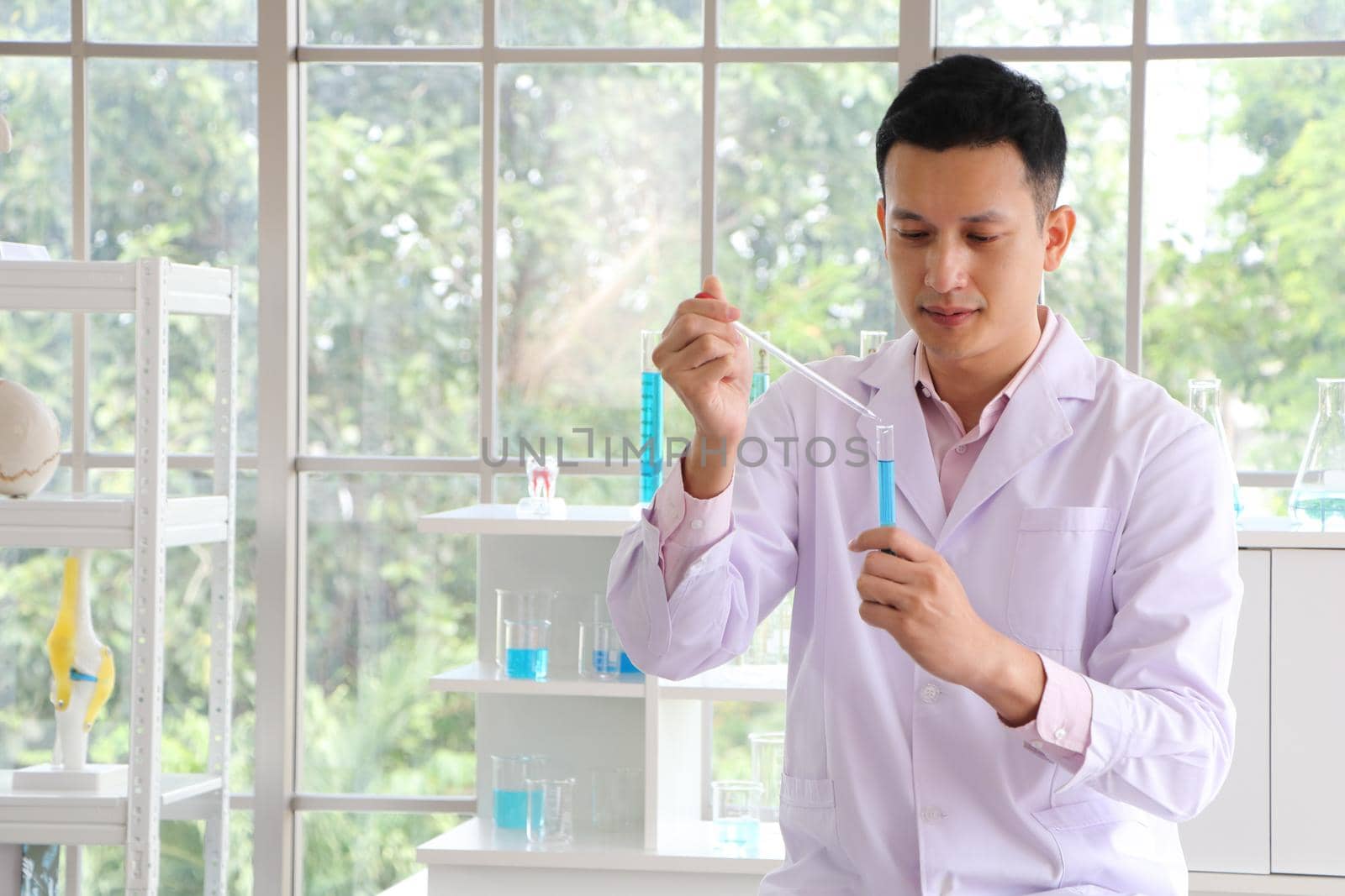 An Asian scientist or chemist drops a blue liquid chemical in a laboratory. Research concepts in healthcare, pharmacy, and medicine. Liquid analysis to separate DNA and molecules in vitro.