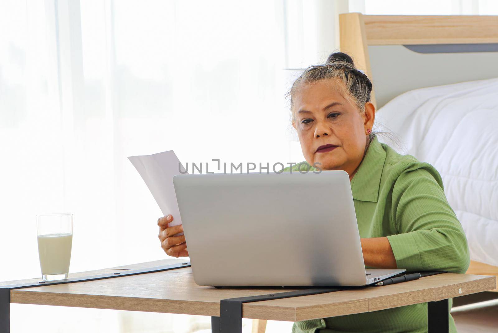 Senior Asian women Carrying documents with a laptop A concept that manages home utility bills or money for older women who use their computers to work or work documents online. Aging and technology