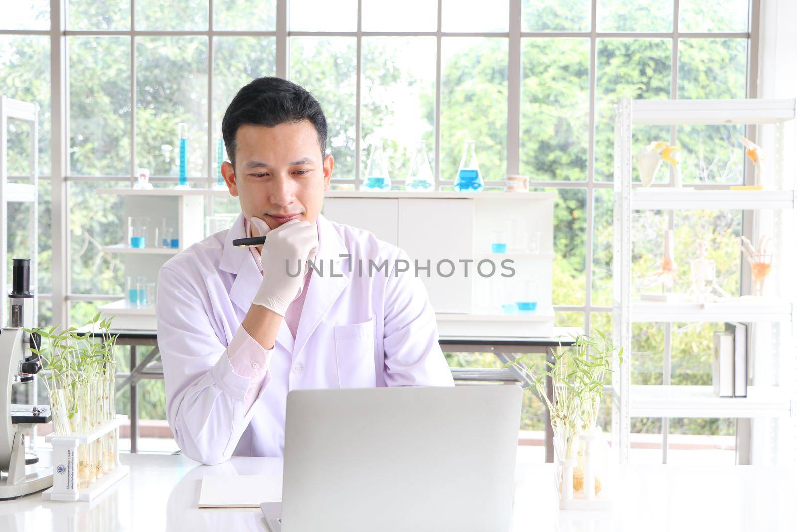 Asian researchers in white coats The concept of working in a scientific laboratory Using a laptop to find information And write down in the test results book Or making a report in a science laboratory