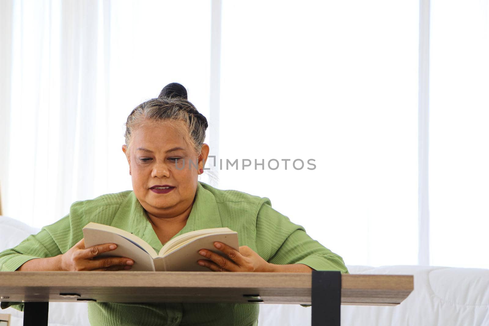 Senior Asian women Retirement Asians Sit and read movies and media at the wooden table in the bedroom. The concept of a relaxed retirement life Enjoy happy