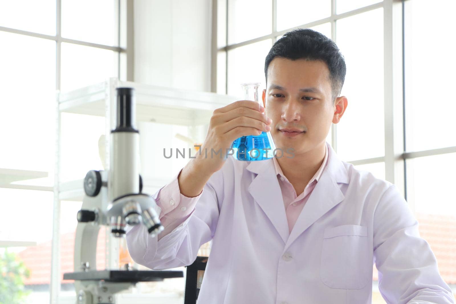 Asian scientist or chemist looks at a blue liquid chemical test tube in the laboratory. Research concepts in healthcare, pharmacy, and medicine. Liquid analysis to separate DNA and molecules in vitro.