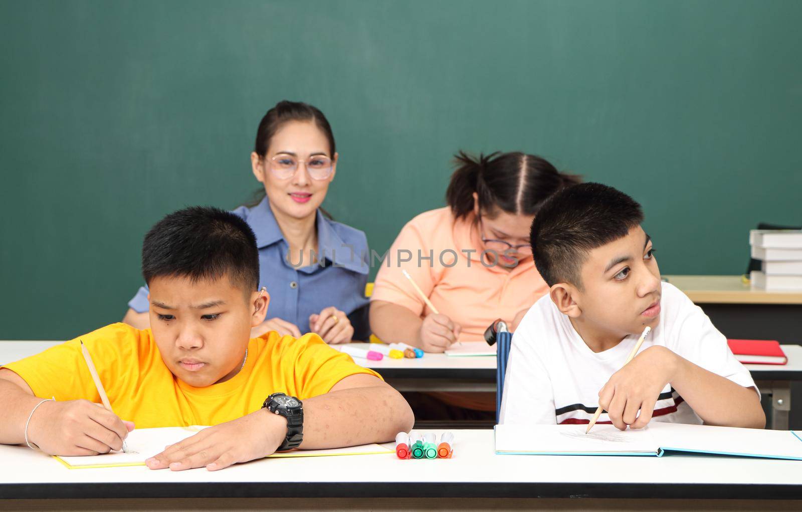 Asian disabled children Or, an autistic child learns to read, write, and train their hand and finger muscles with a teacher at their classroom desk. Concentrate and smile Happy disability kid concept