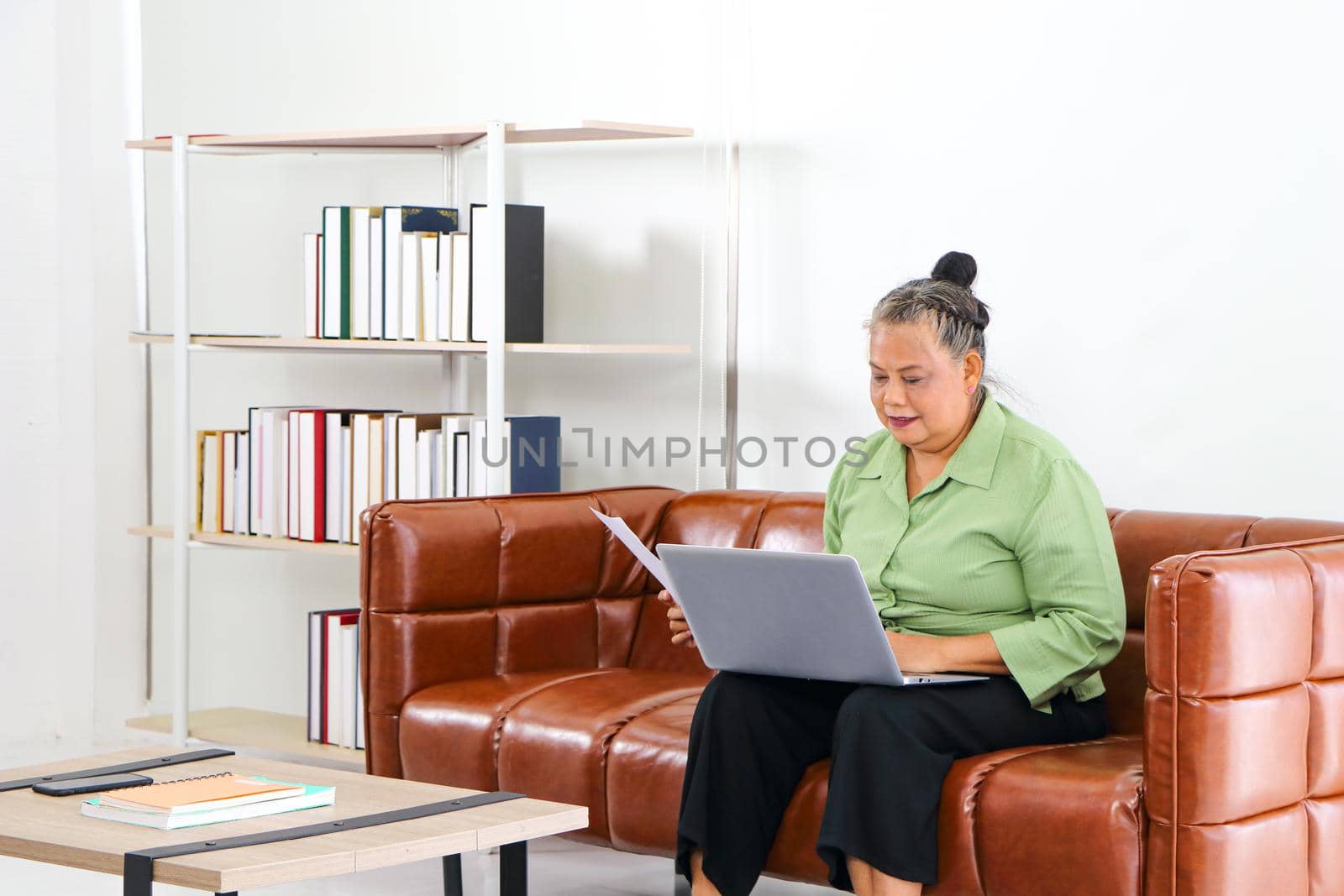 Asian women Retirement Use a smartphone and laptop in the living room concept to work at home. Quarantine to prevent spreading disease Or a conversation with someone far away Via the Internet