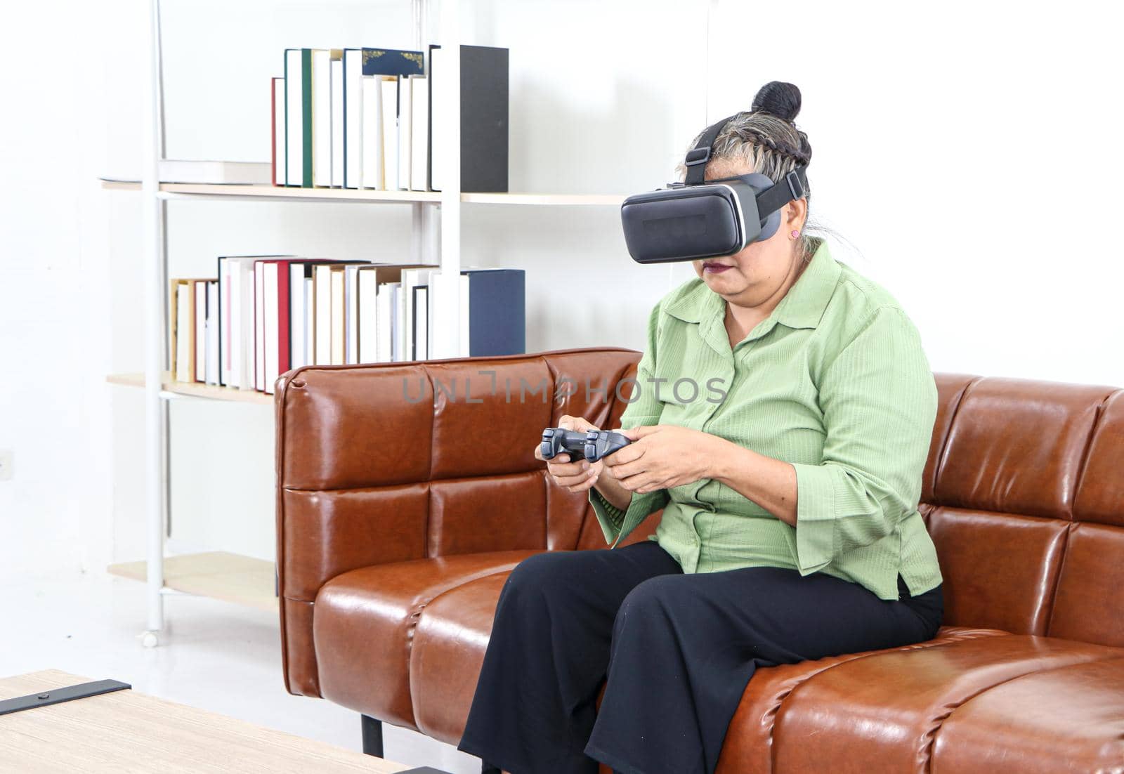 Retired Asian women are enjoying VR  glasses for advanced augmented reality headsets in an amazing 3D format on the couch, the concept of technological innovation, and relaxing fun. For adults at home