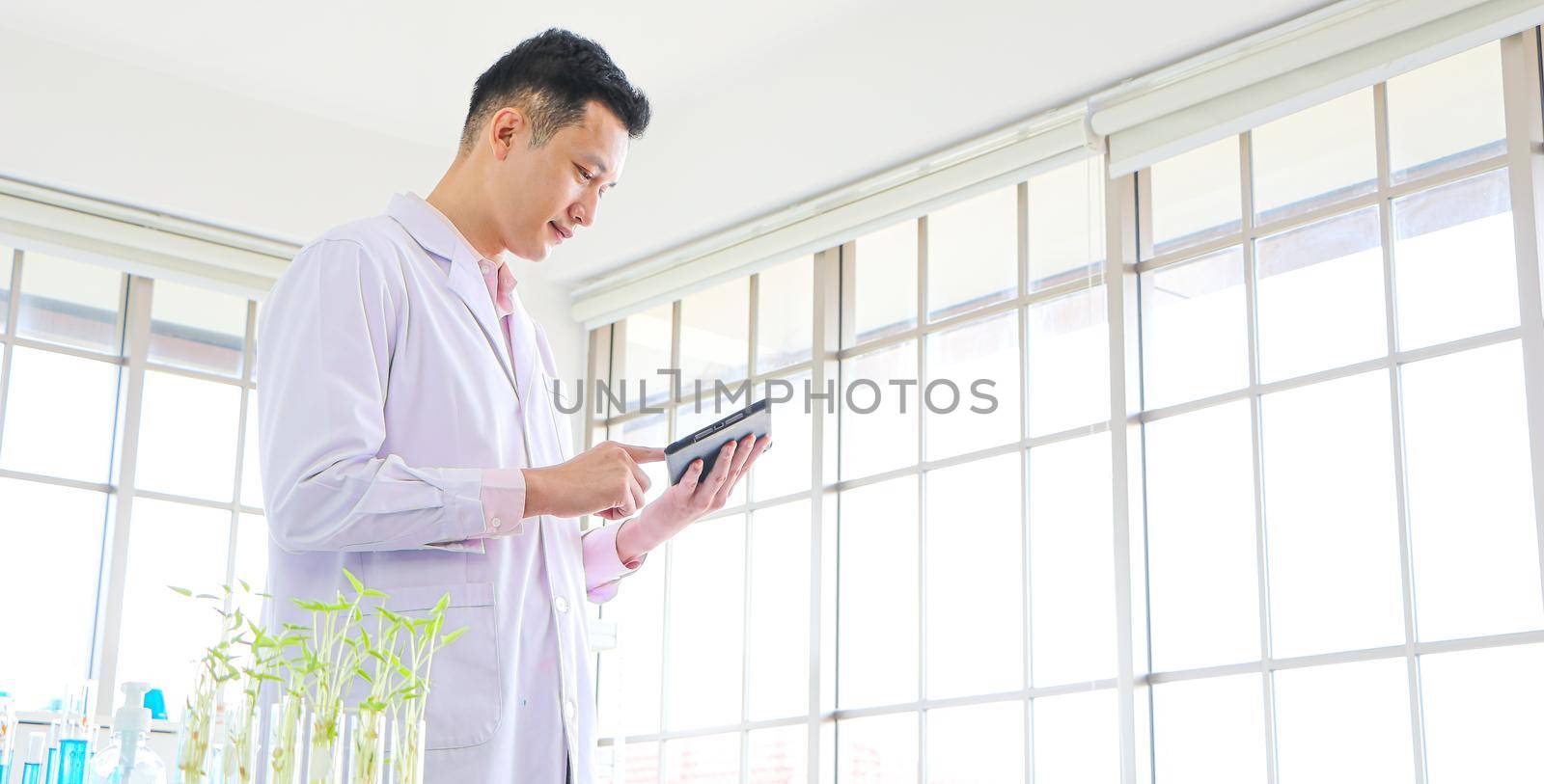 An Asian scientist or researcher wearing white clothes. He carried a tablet with a science lab and Laboratory test tubes during working hours In the concept of corona vaccine research and development