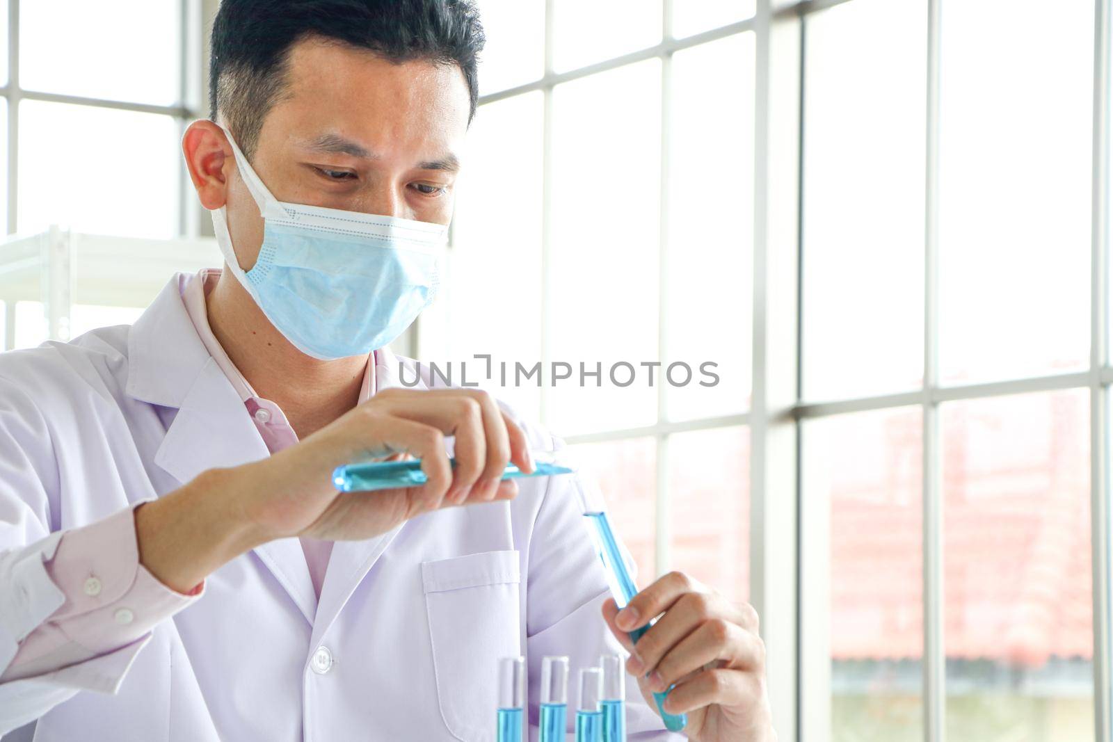 An Asian scientist or chemist drops a blue liquid chemical in a laboratory. Research concepts in healthcare, pharmacy, and medicine. Liquid analysis to separate DNA and molecules in vitro.