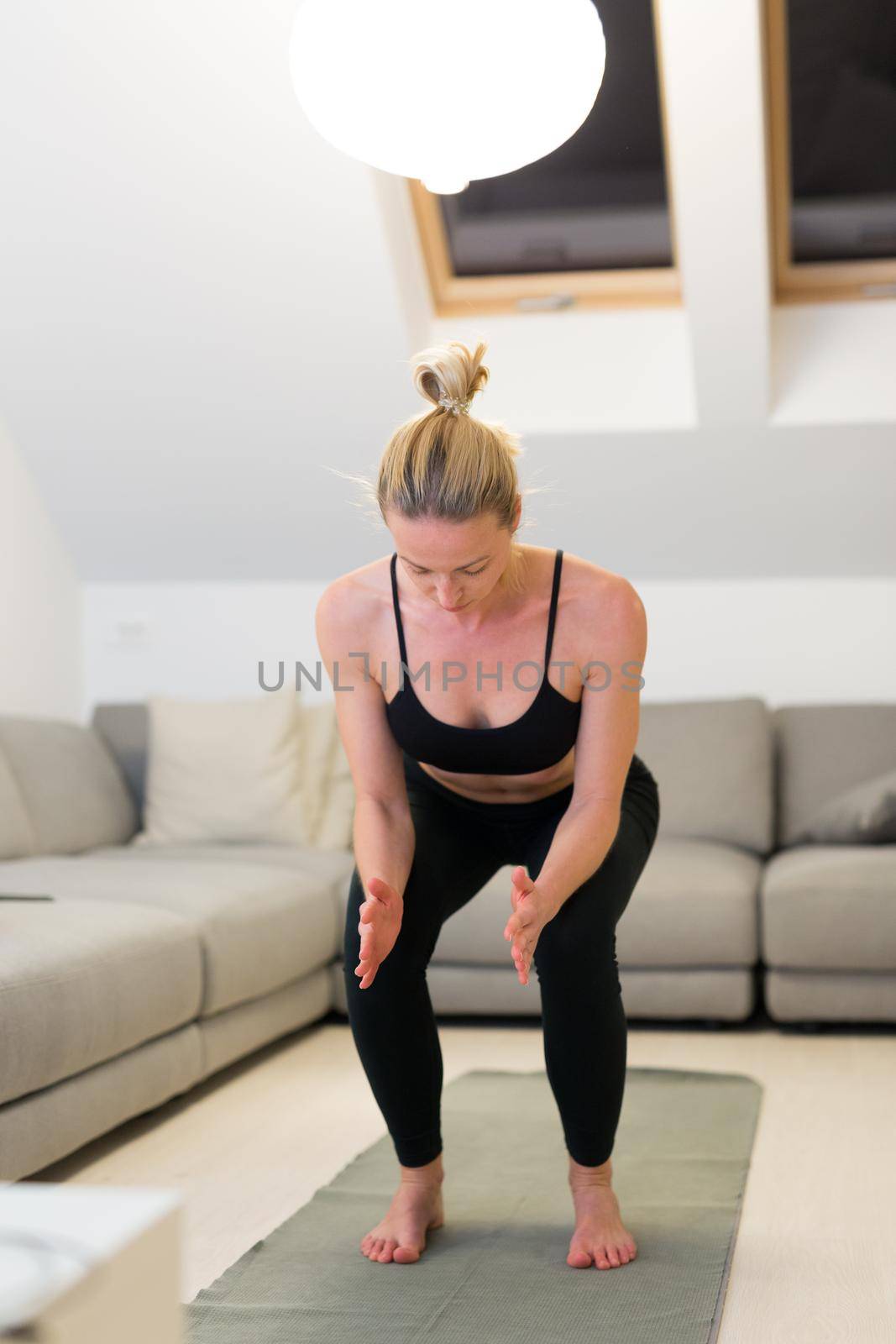 Beautiful blonde woman doing home workout indoors. Woman practice yoga at home. Fit girl using workout tutorials for healthy active lifestyle. Woman using quarantine for home workouts. Stretching