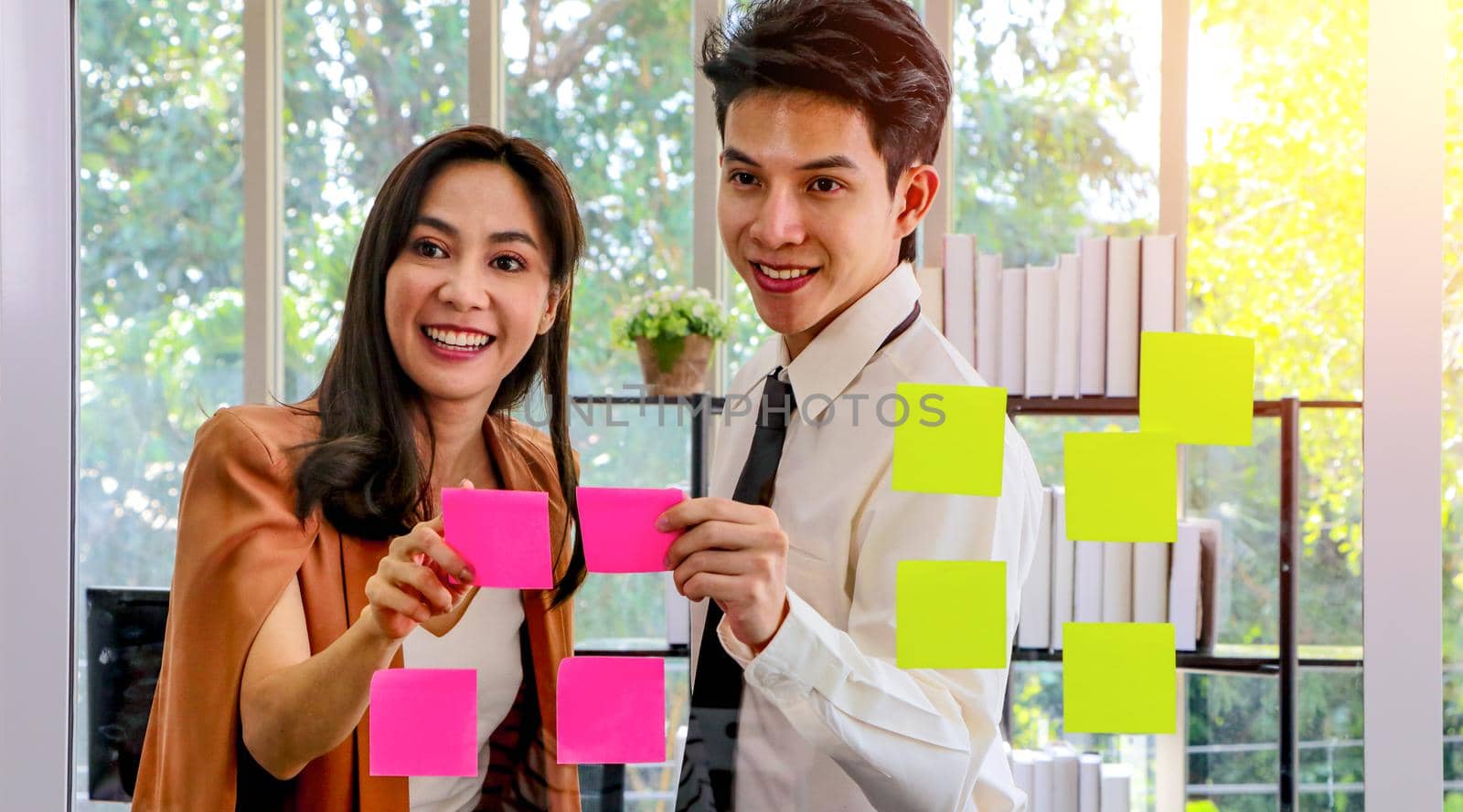 Asian businessmen and women looking and writing post-it notes for brainstorming. Put a post on the mirror in the office Work plan, brainstorm, strategy Creative Lifestyle, Success in Business Concept