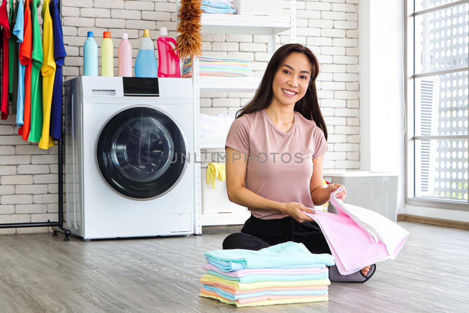 Asian woman sitting in the laundry room She picked up the folded laundry and checked the cleanliness after the washing machine finished. Smile and happiness