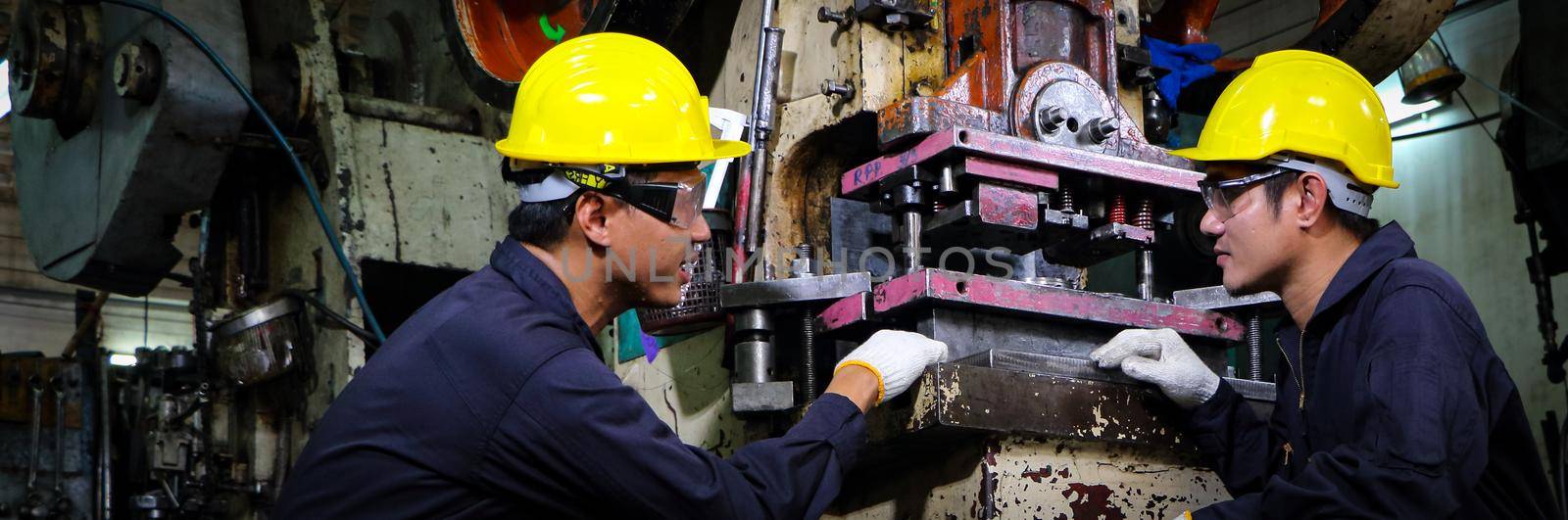 Two skilled Asian workers, dressed in helmet uniforms, were talking to analyze the inspection data. Maintenance of metal printing press The concept of teamwork at the factory