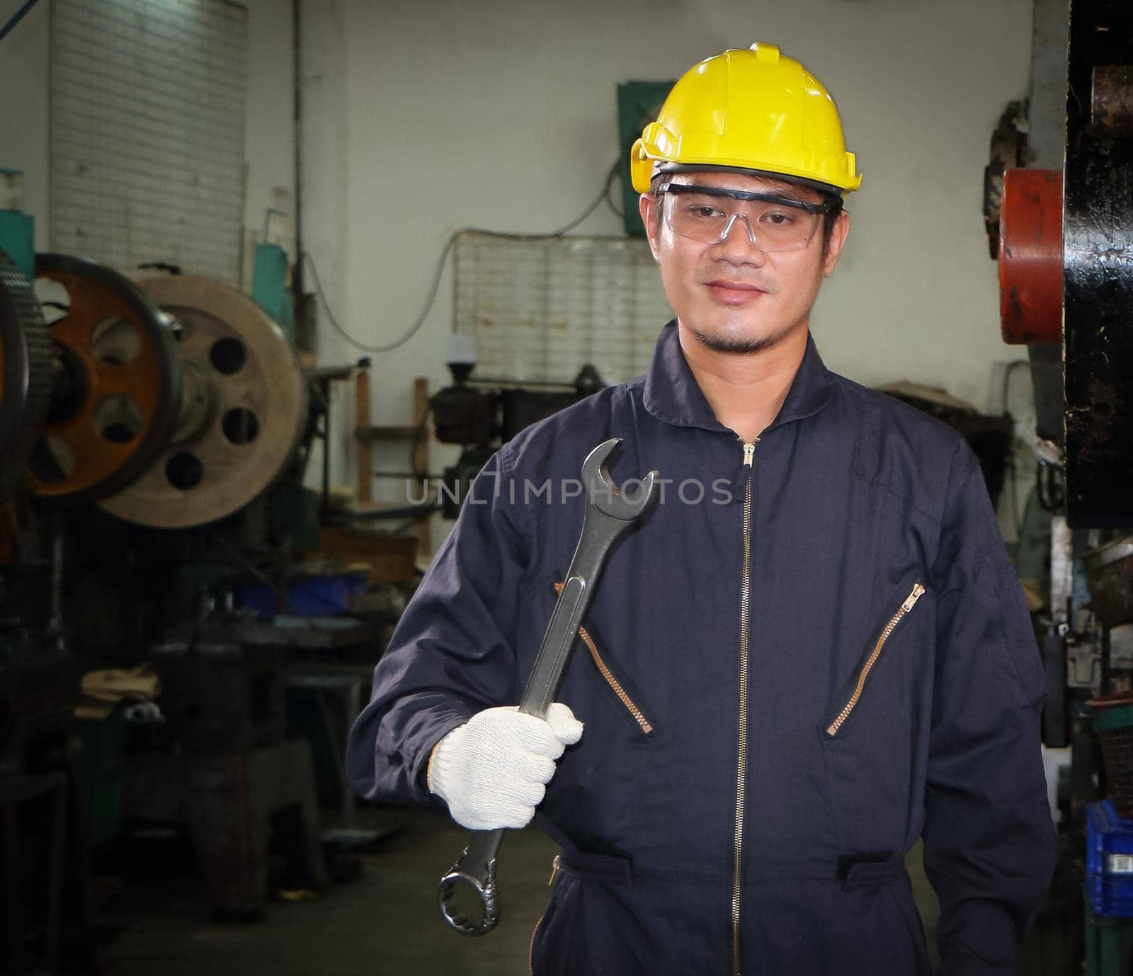 Asian male worker In industries that wear glasses, safety hats and safety uniforms Wrench tool holder stand Machine maintenance technician concept In the industry with confidence