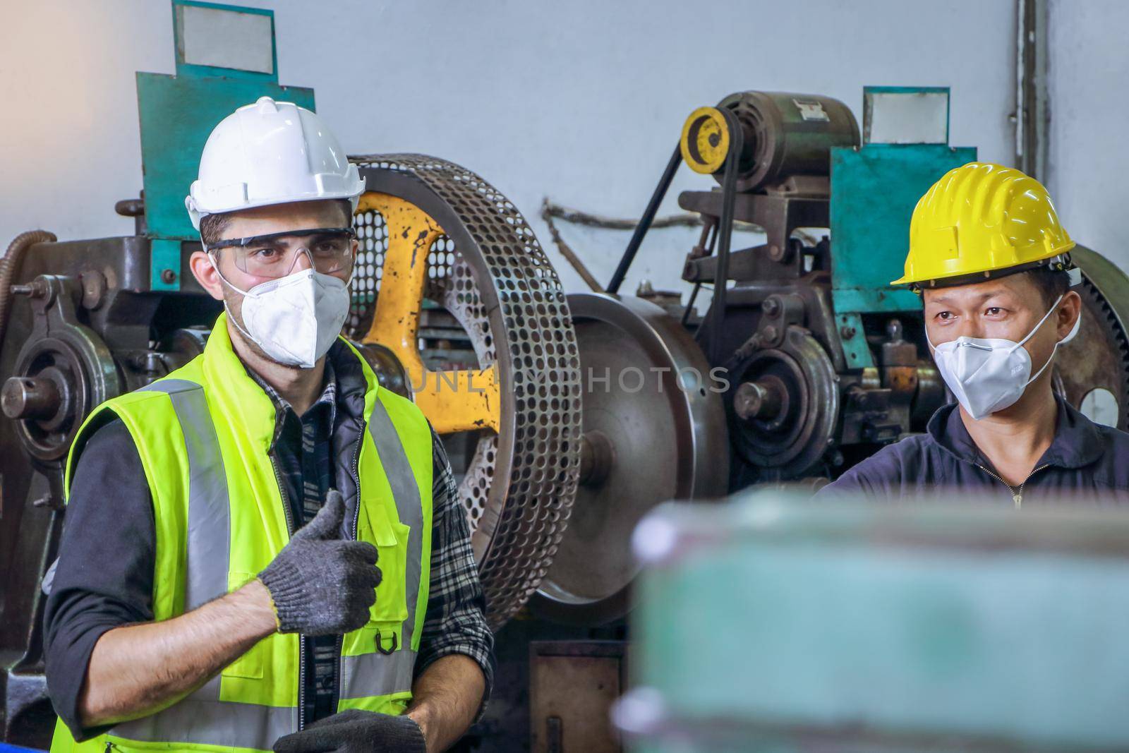 Professional technicians wearing safety clothing Face mask, standing, holding a safety hat. Mechanical engineering concept. Heavy industrial work on metalwork at machines for steel structure industry.