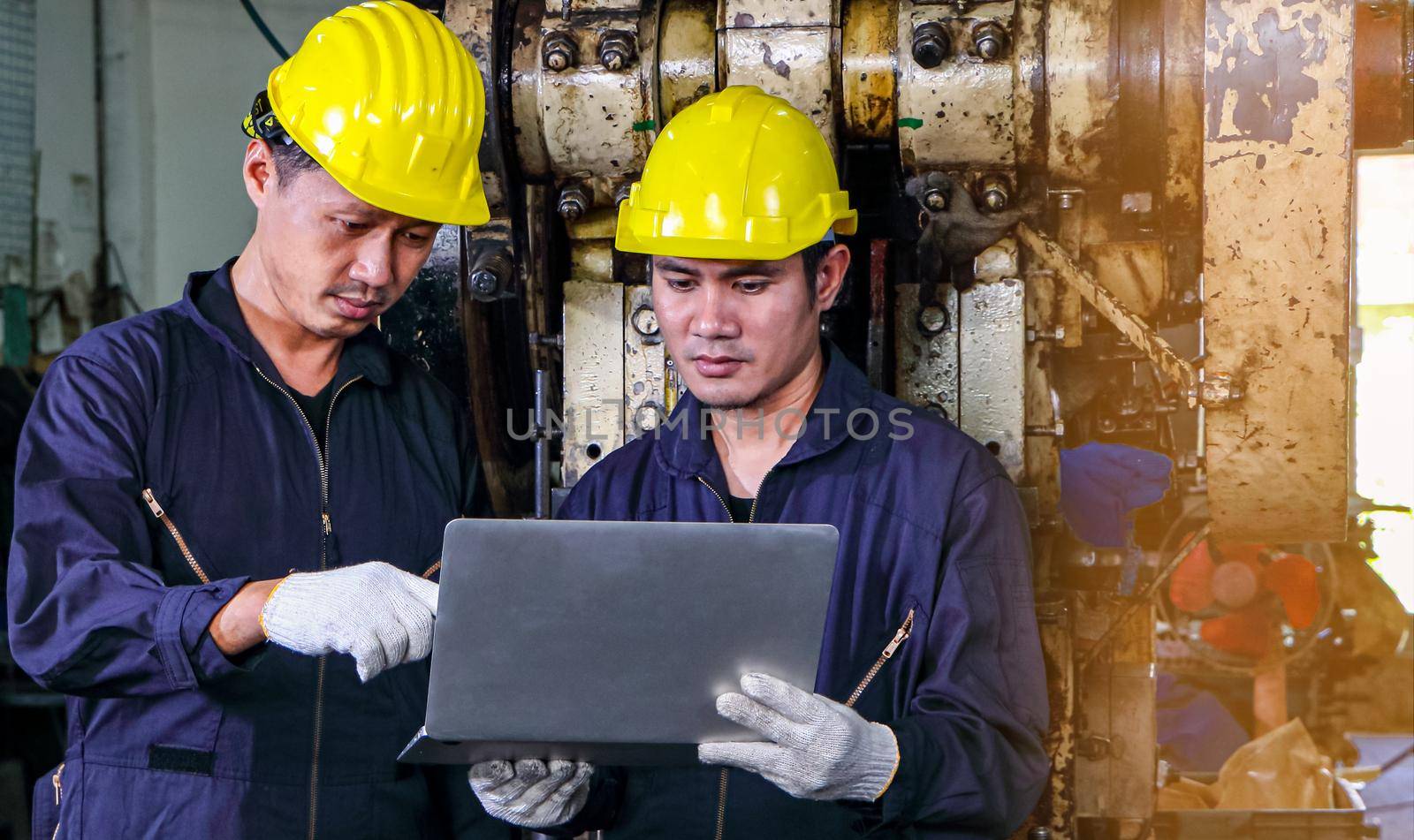 Two skilled Asian workers, dressed in helmet uniforms, were using a computer. by atitaph