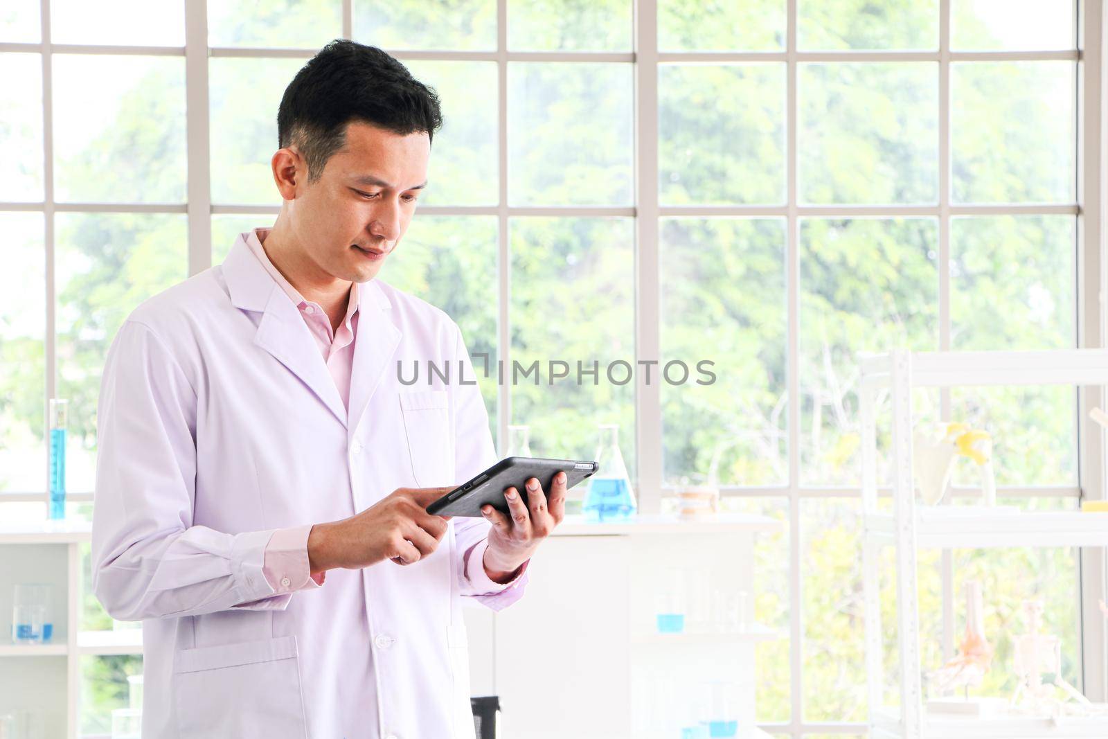 An Asian scientist or researcher wearing white clothes. He carried a tablet with a science lab and Laboratory test tubes during working hours In the concept of corona vaccine research and development