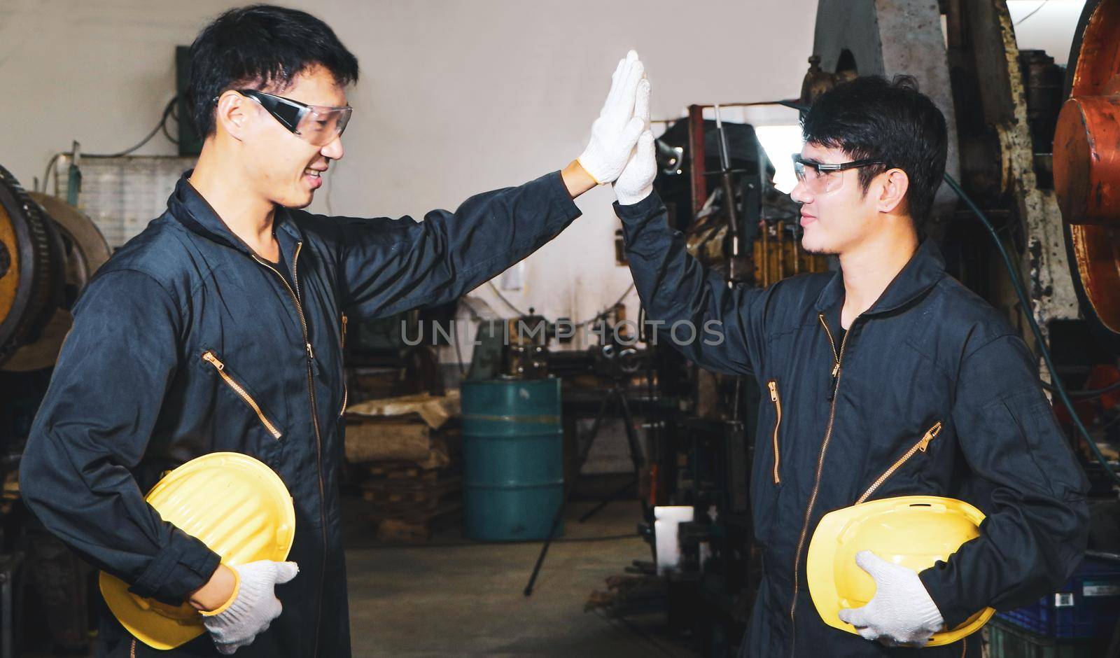 Two skilled Asian workers in uniforms were talking and touching each other with their hands. When the work is done In the maintenance of the metal press, the concept of teamwork at the factory.