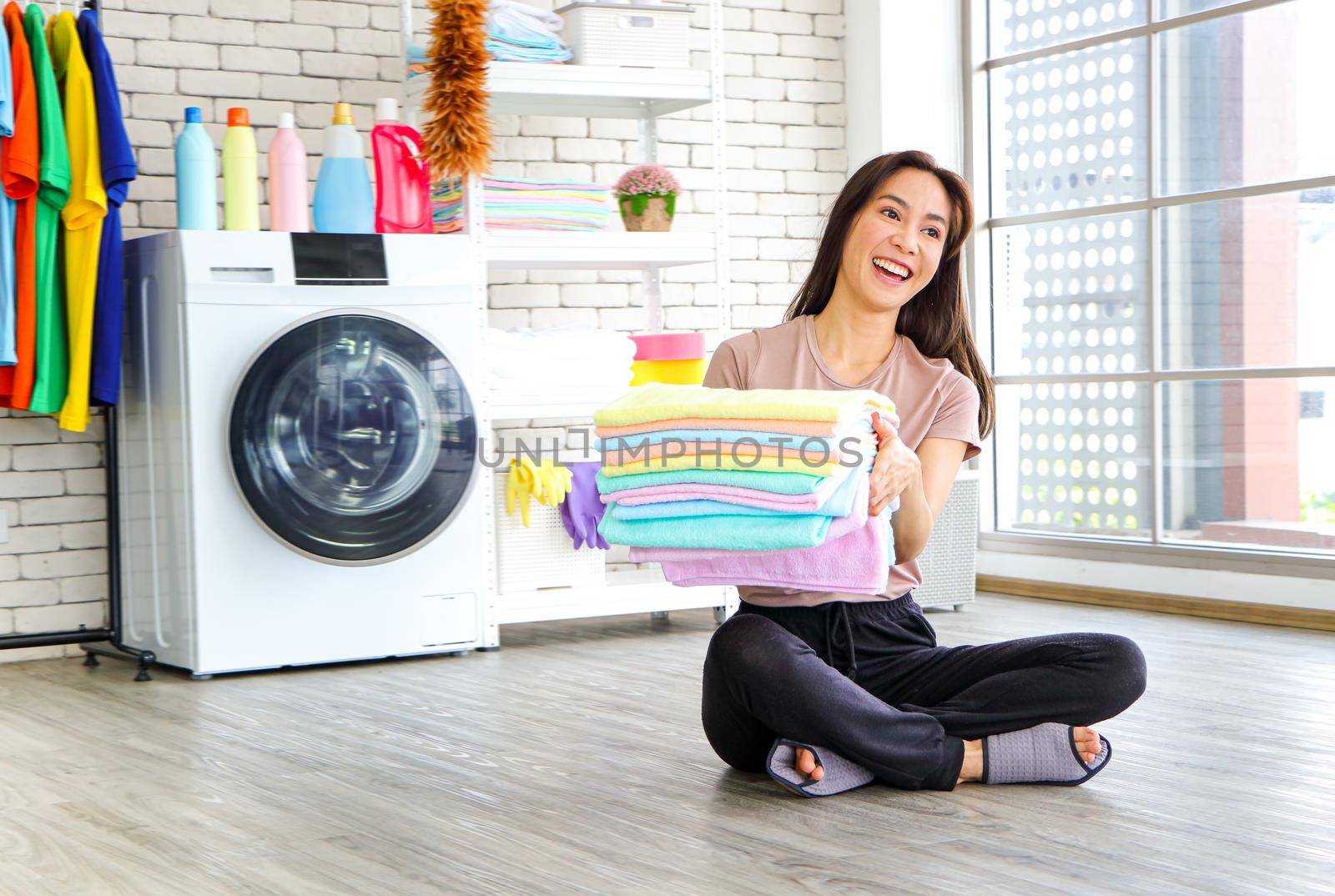 Asian woman sitting in the laundry room She picked up the folded laundry and checked the cleanliness after the washing machine finished. Smile and happiness