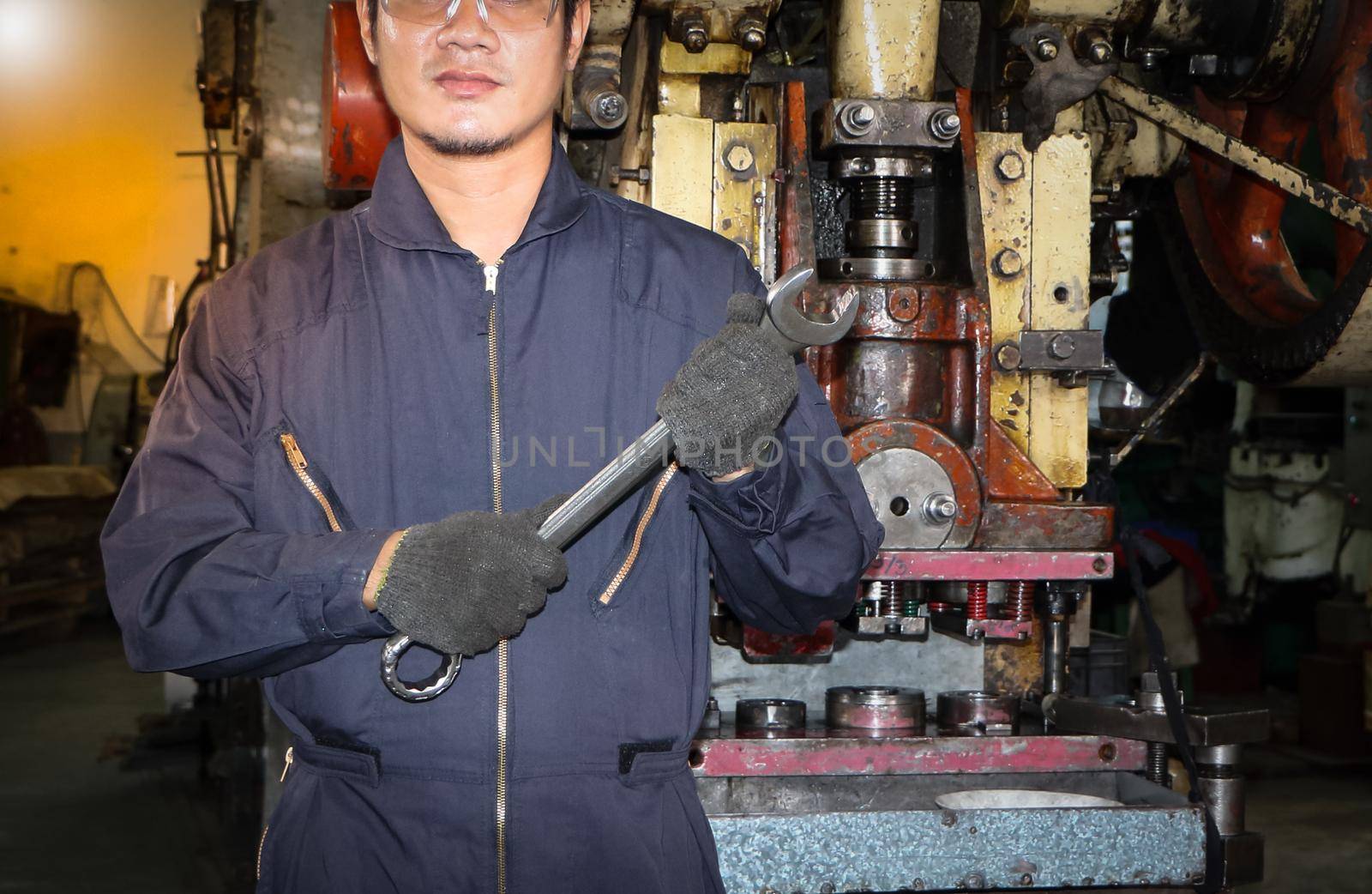 Asian male worker In industries that wear glasses, safety hats and safety uniforms Wrench tool holder stand Machine maintenance technician concept In the industry with confidence