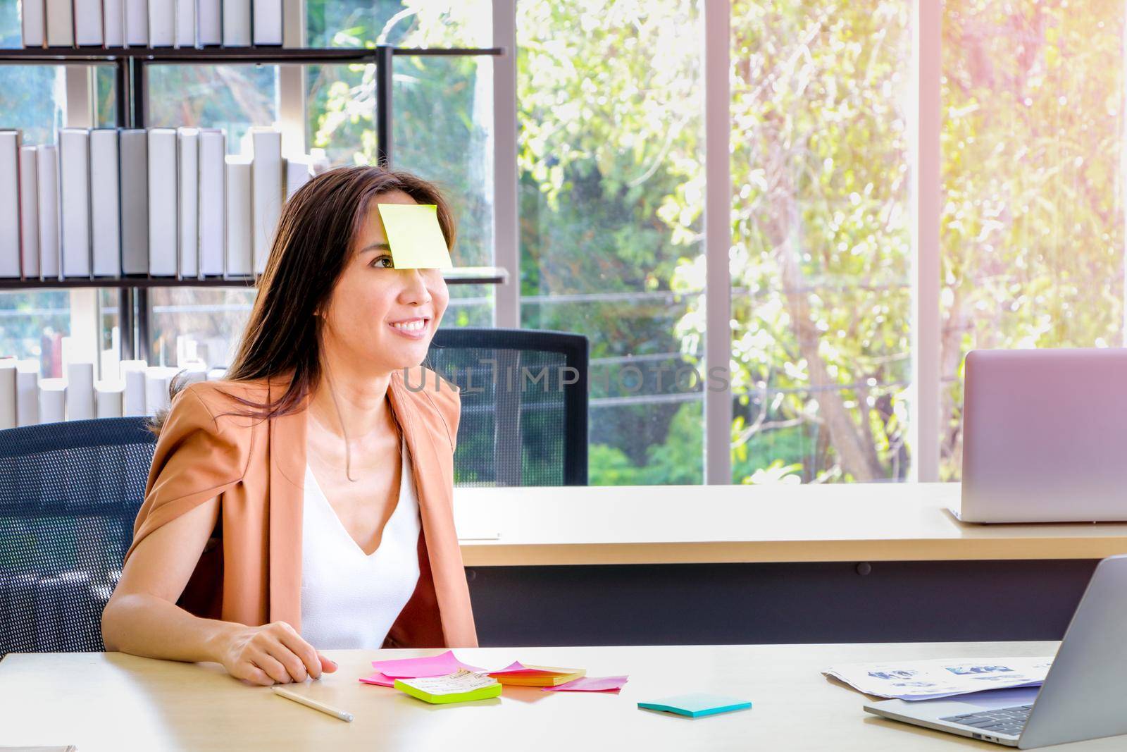 Asian businesswomen look and write a post-it note on their faces to relax and smile from work. Work plan, brainstorm, strategy Creative Lifestyle, Success in Business Concept