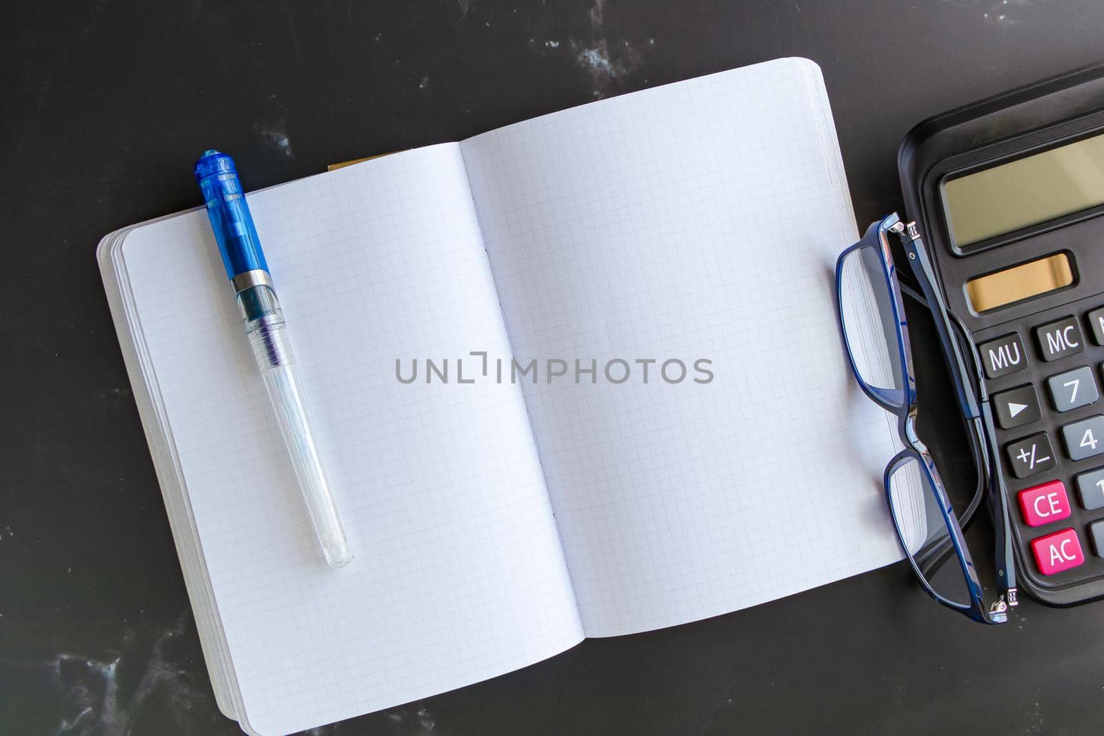 Top view Blank Notebook Calculator and glasses on a black marble table background. Simple financial business concepts, working at home or office for social distancing measures, plus copy space.