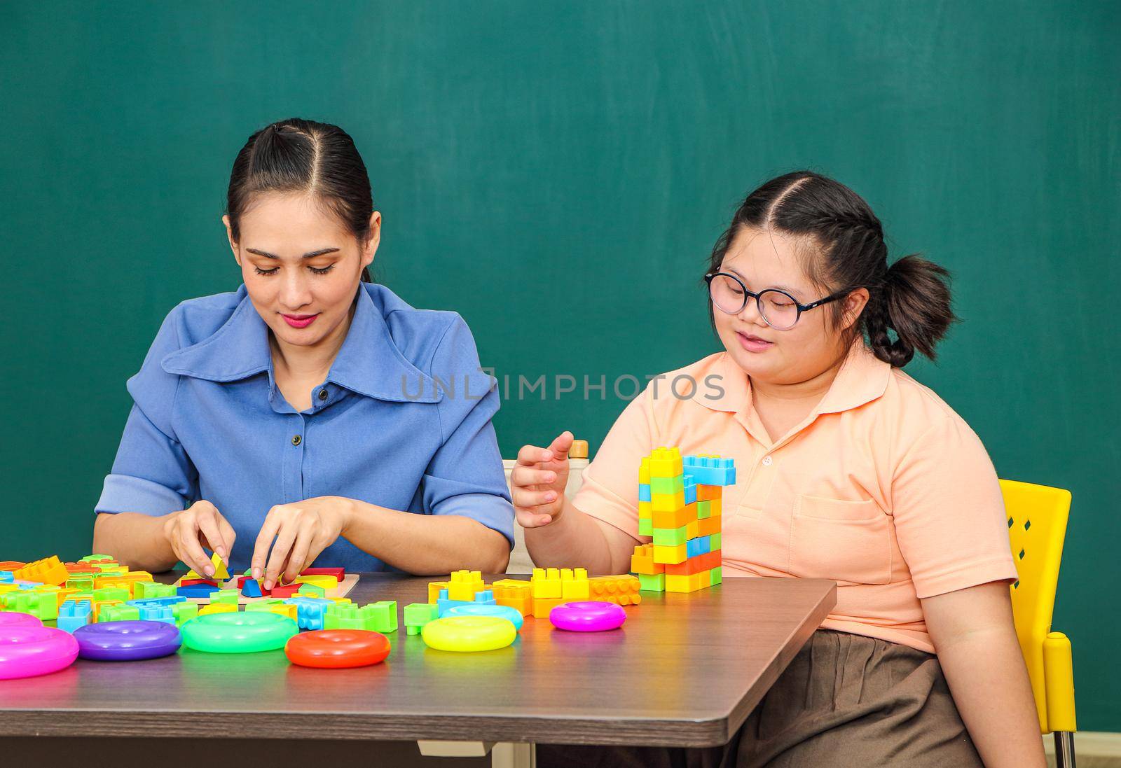 An Asian girl with a disability is practicing the use of hand and finger muscles. By playing with toys With a helping teacher to care for happiness and concentration in the classroom