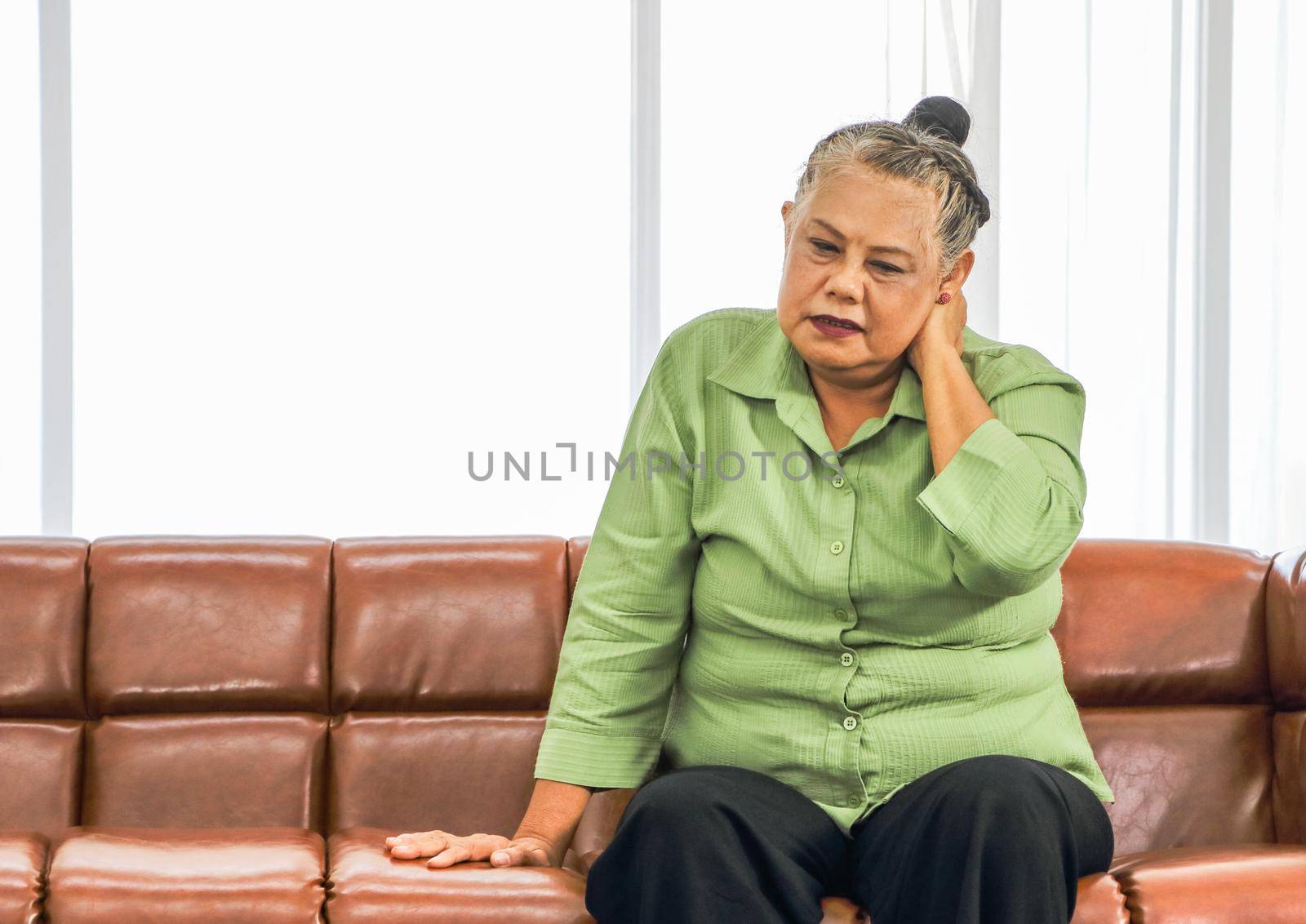 Asian elderly woman Grasping the head in pain while sitting on the sofa in the room Health care concept Women suffering from headaches Senior female health problems and people's concepts