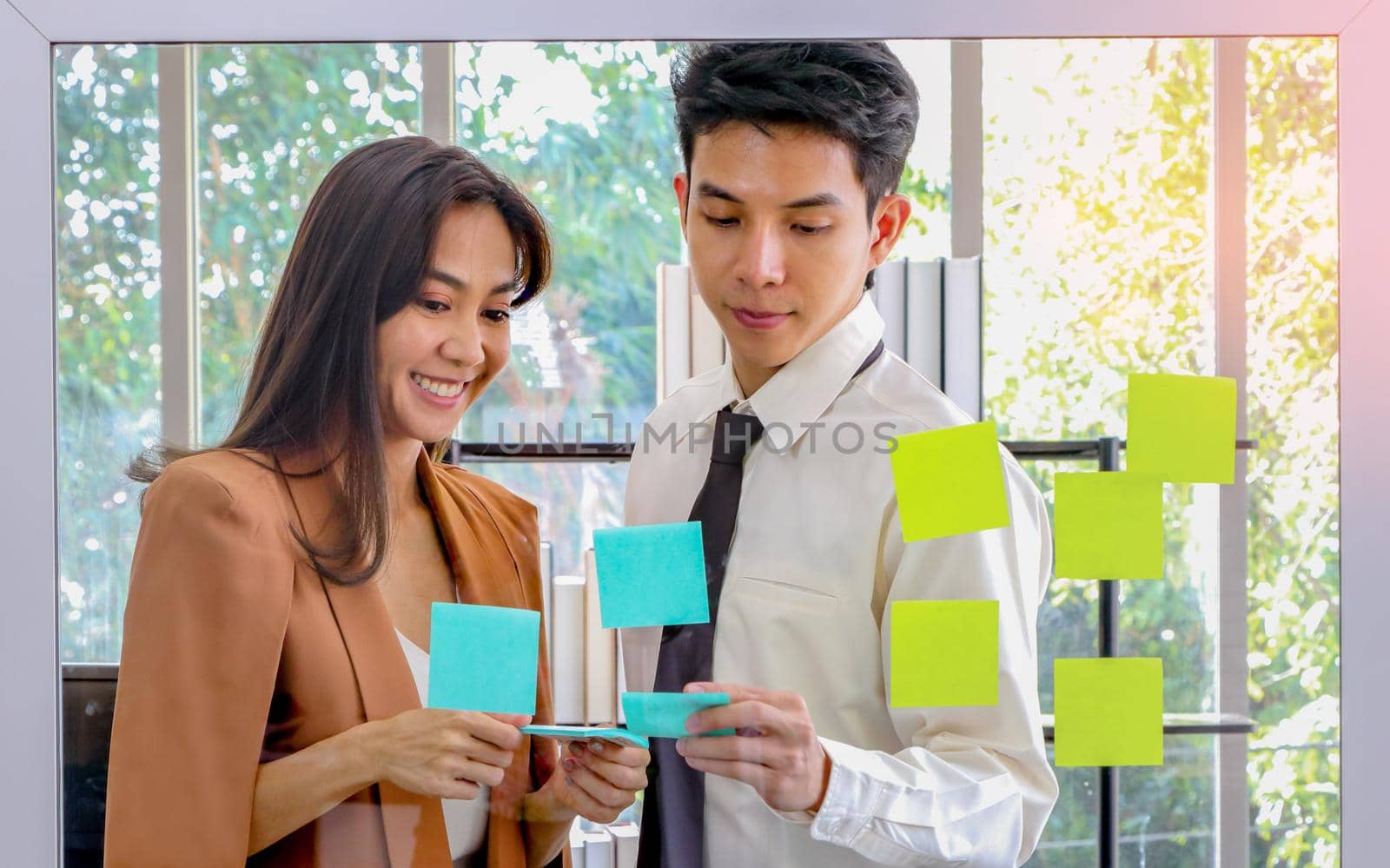 Asian businessmen and women looking and writing post-it notes for brainstorming. Put a post on the mirror in the office Work plan, brainstorm, strategy Creative Lifestyle, Success in Business Concept