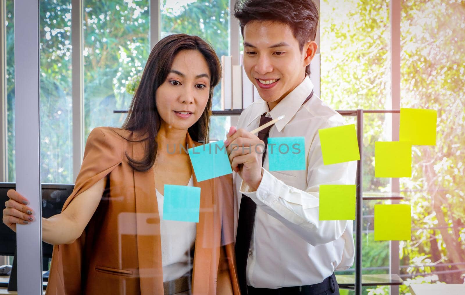 Asian businessmen and women looking and writing post-it notes for brainstorming. Put a post on the mirror in the office Work plan, brainstorm, strategy Creative Lifestyle, Success in Business Concept