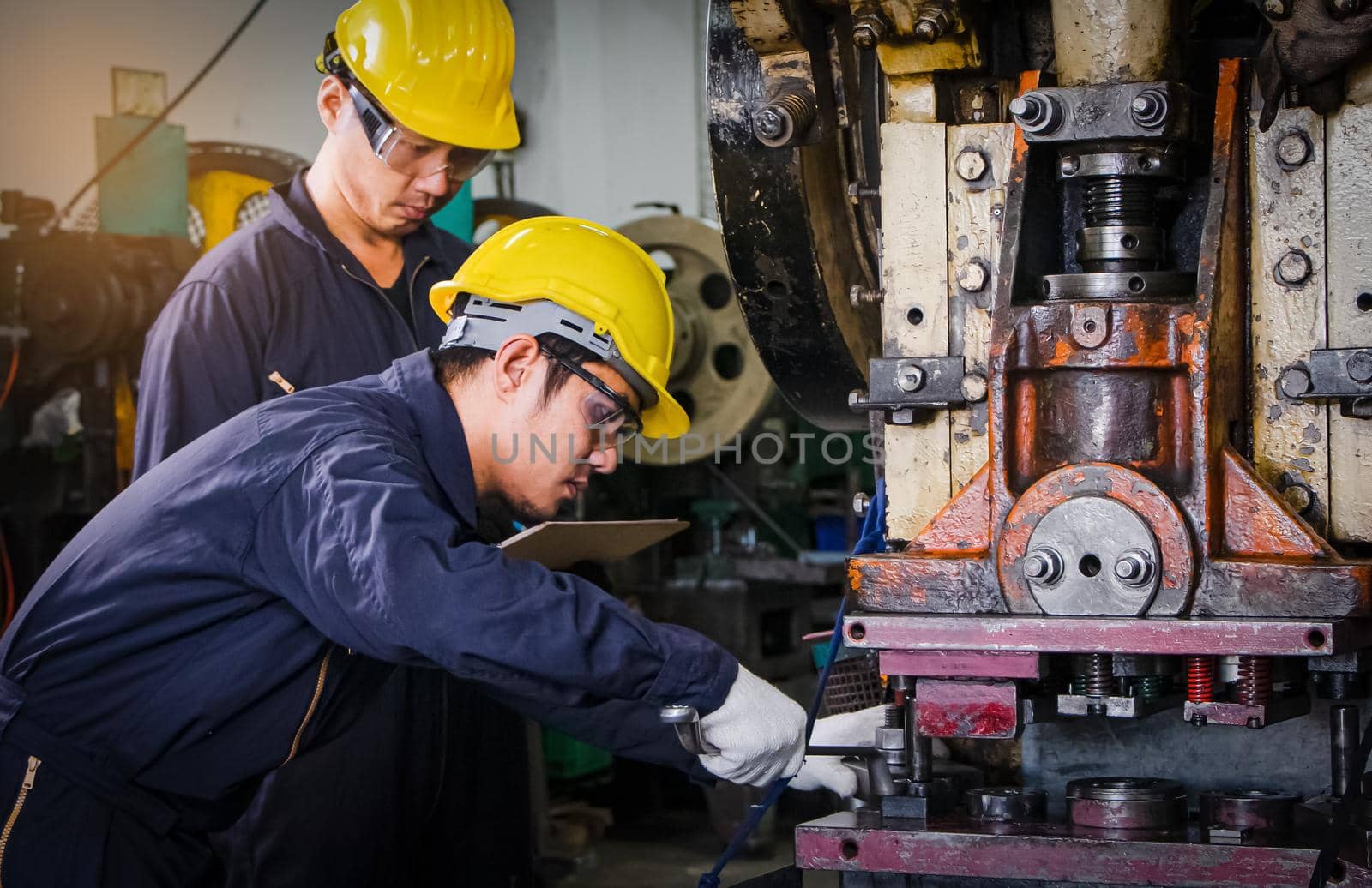 Asian male worker In industries that wear glasses, safety hats and safety uniforms Wrench tool holder stand Machine maintenance technician operation concept In an industrial factory with confidence