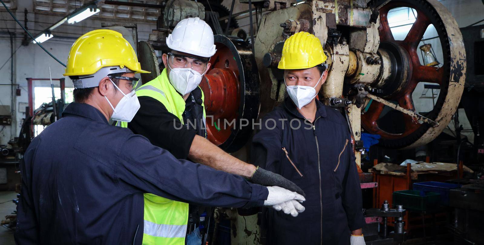 Two skilled Asian workers in uniforms were talking and touching each other with their hands. When the work is done In the maintenance of the metal press, the concept of teamwork at the factory.