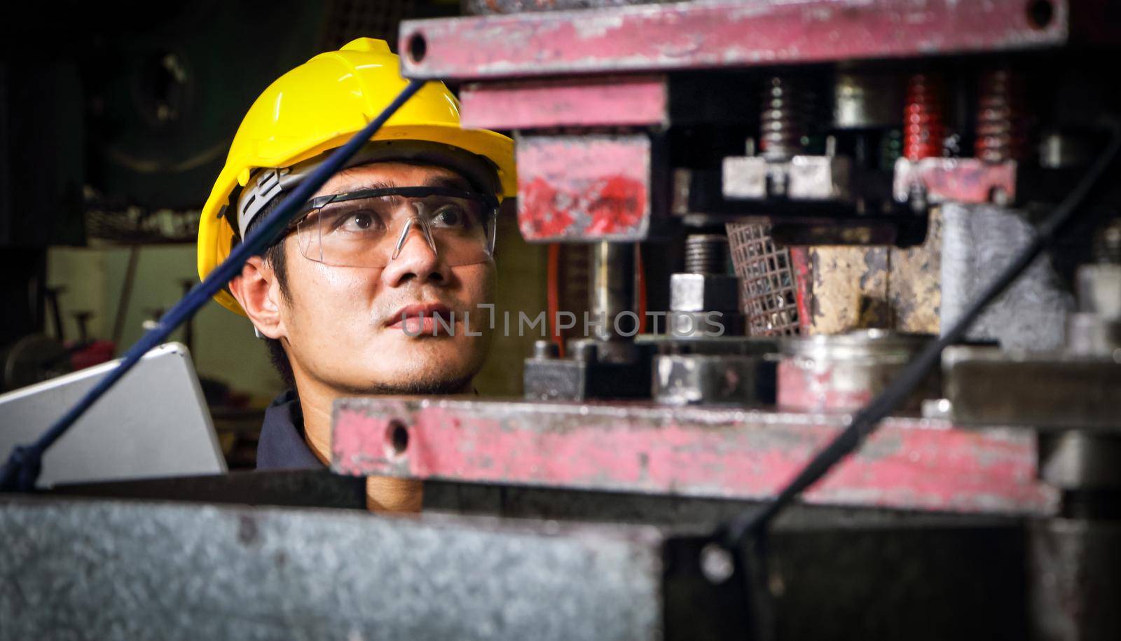 Skilled Asian workers wearing uniform clothing, safety hats, and safety goggles. Are using a tablet to analyze data Metal press maintenance inspection at the factory, concept